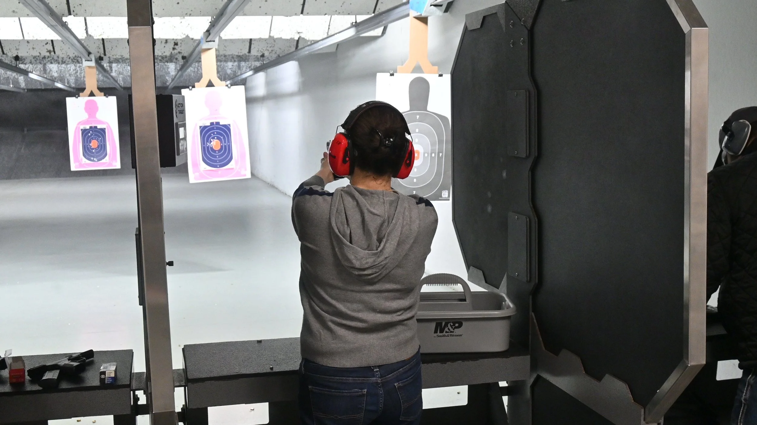 Individual at an indoor shooting range aiming at targets wearing ear protection, with multiple targets visible in the background.