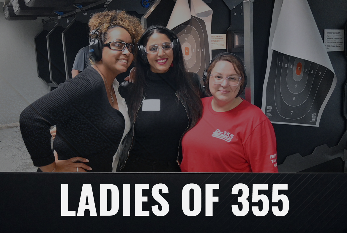 Three women wearing safety glasses and ear protection pose at a shooting range with target targets in the background. The woman on the right wears a red shirt with the text 'B-455' and a fire department logo.