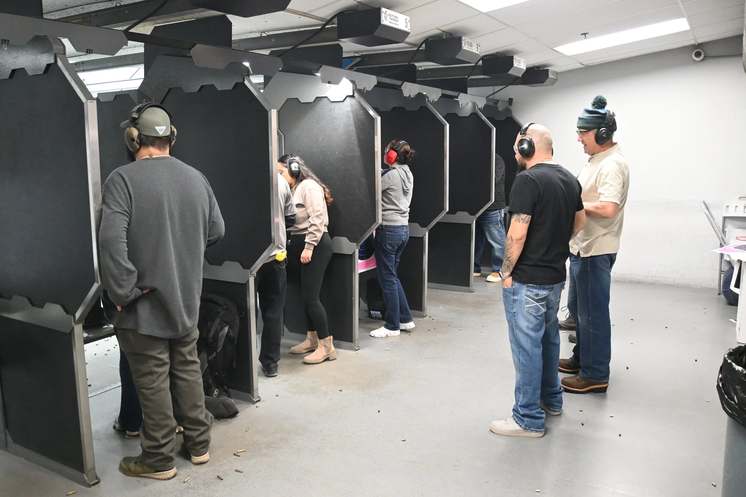 People at a shooting range, aiming at targets in individual booths, wearing ear protection.
