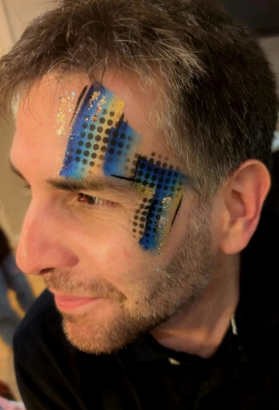 Man with blue and black geometric design facepaint on temple