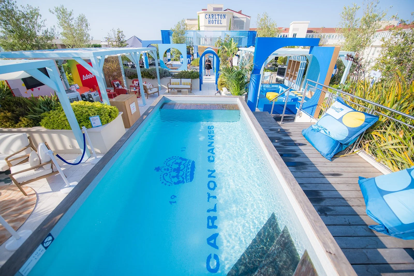 Outdoor rooftop pool area at Carlton Hotel with lounge chairs, umbrellas, and surrounding greenery in bright, sunny weather. Event Photography by Carl Thomson