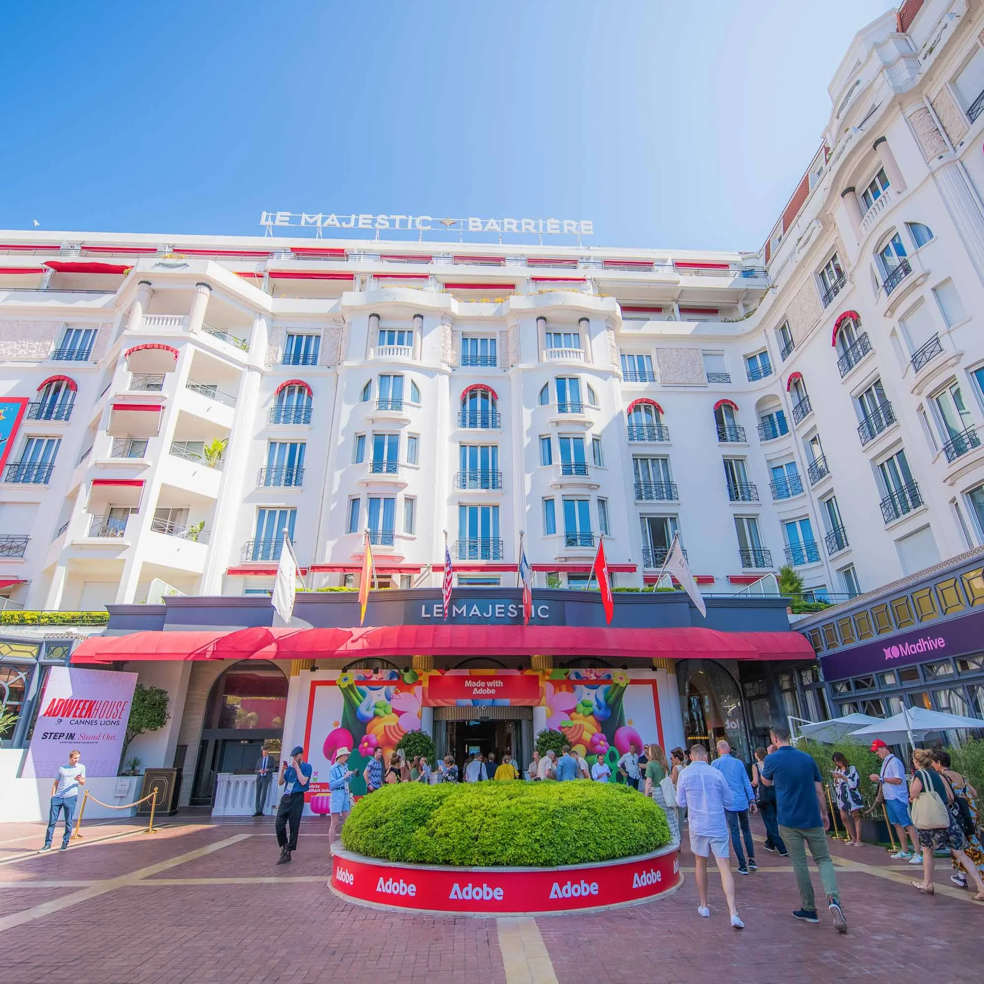 Crowd of people entering the Le Majestic hotel at the Cannes Film Festival, with banners of Adobe and colorful decorations in front.