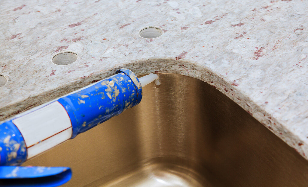 Someone adding caulk to a kitchen countertop and sink connection point