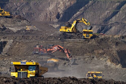 A zoom-in on a cole mining site with 5 yellow vehilces, one yellow digger and an orange digger.jpeg