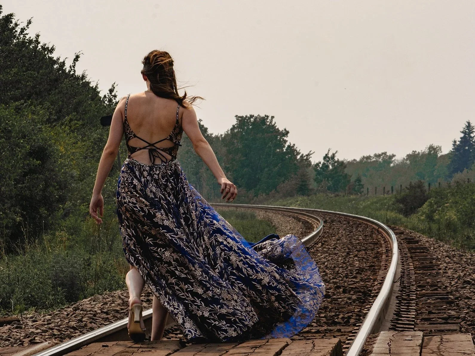A woman in a long, flowing dress walking on train tracks outdoors.