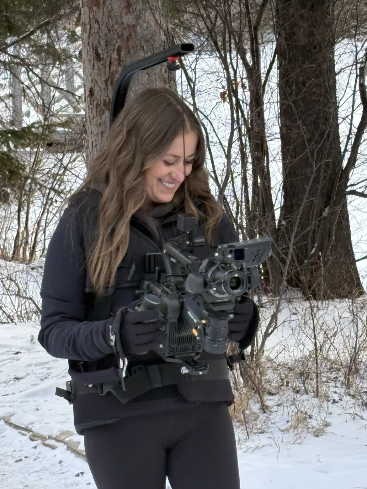 A woman holding a camera in a snowy outdoor setting with trees in the background.