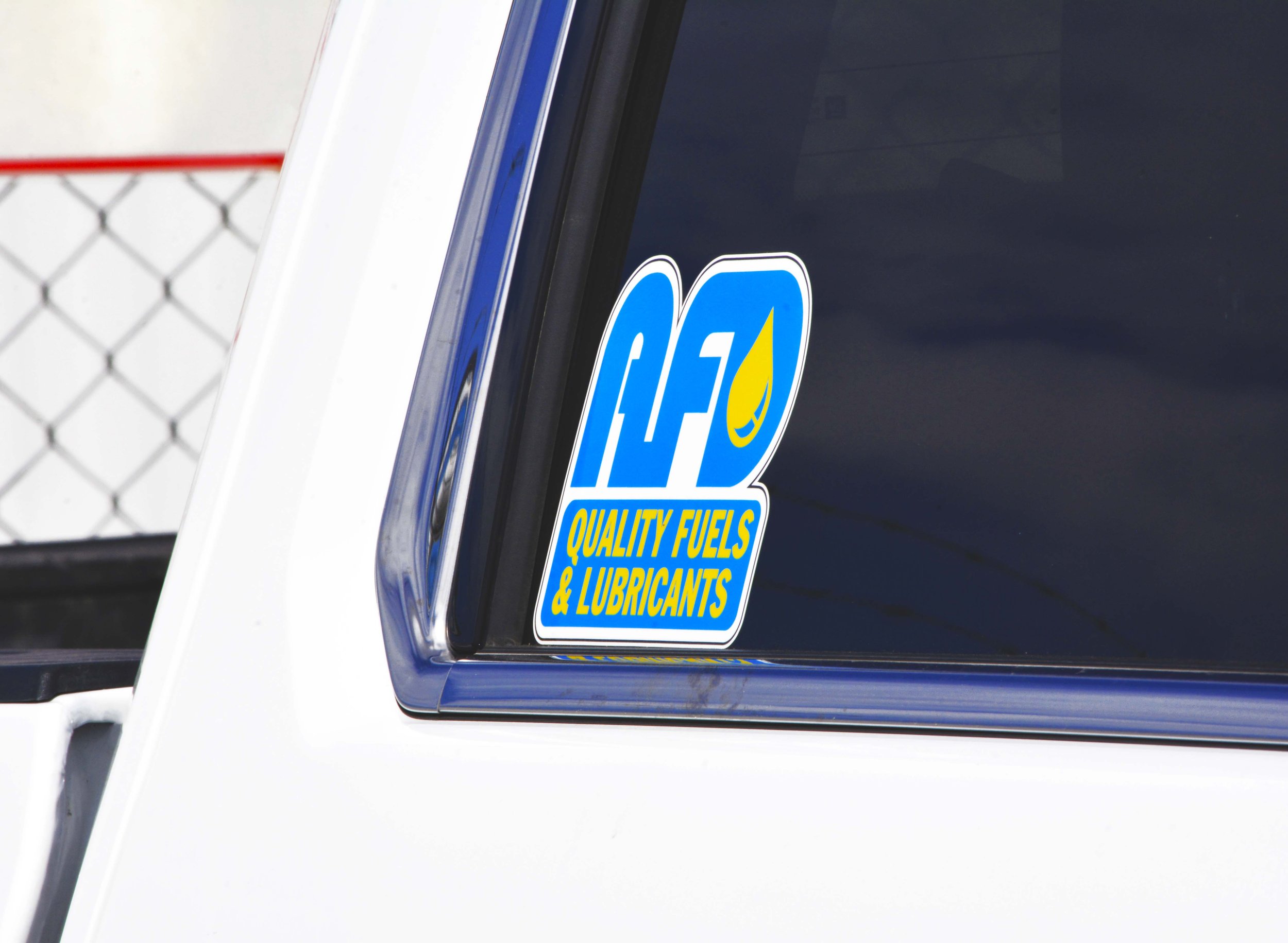 Close-up of a convenience store window displaying a blue and yellow sticker for IFA, a fuel and lubricant company.