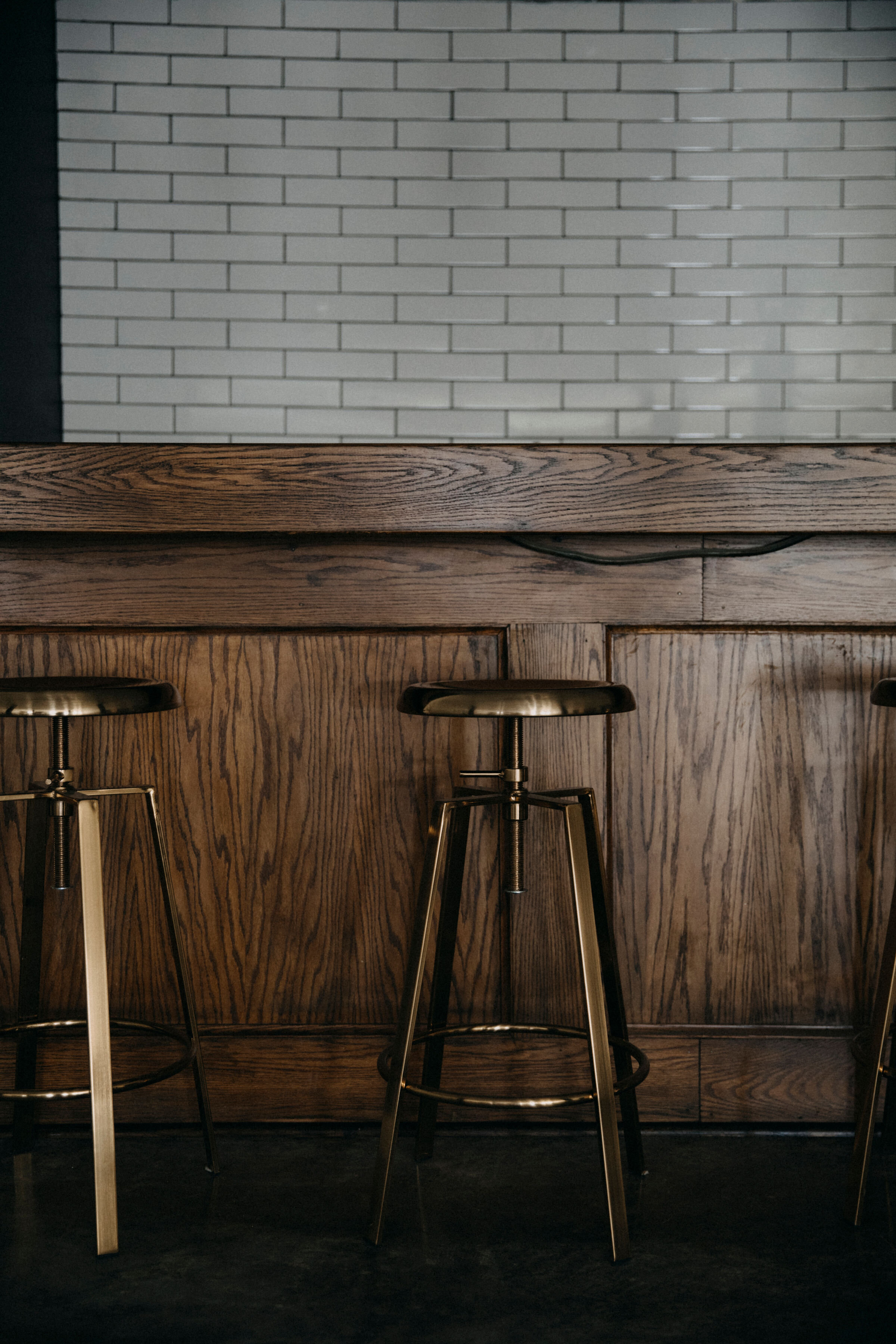 Brass barstools with white subway tile behind the bar