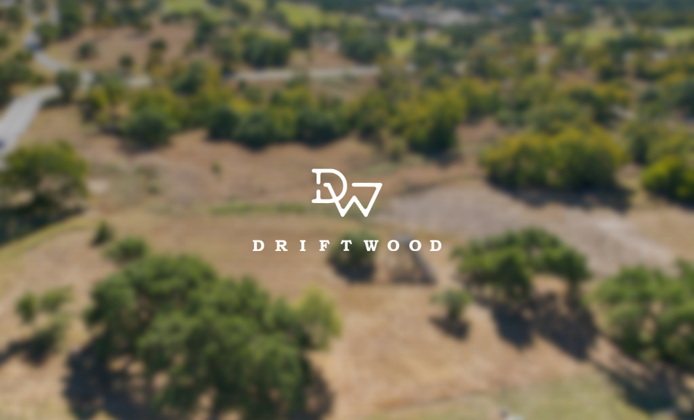 Blurred aerial view of a landscape with trees, hills, and open land, with Driftwood logo overlay.