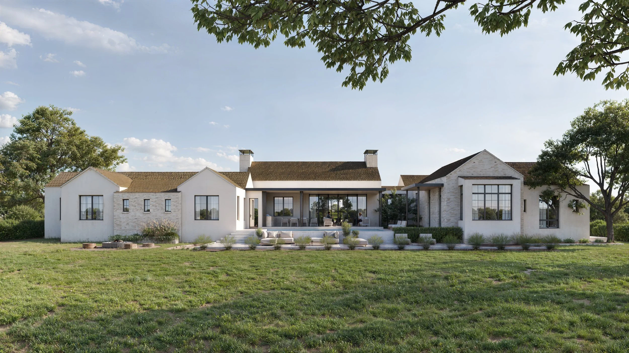 Modern house with white walls, large windows, and a backyard patio with outdoor furniture, surrounded by green grass and trees under a partly cloudy sky.