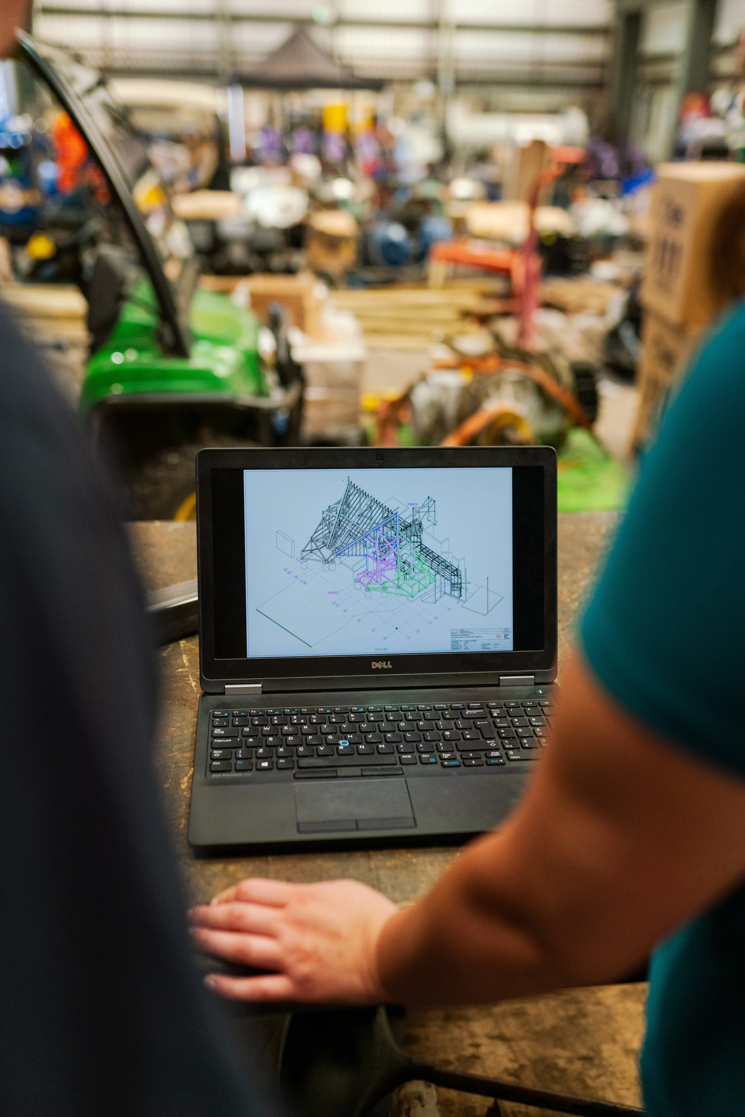 Person working on a laptop with a technical drawing of a structure on the screen in an industrial warehouse setting.