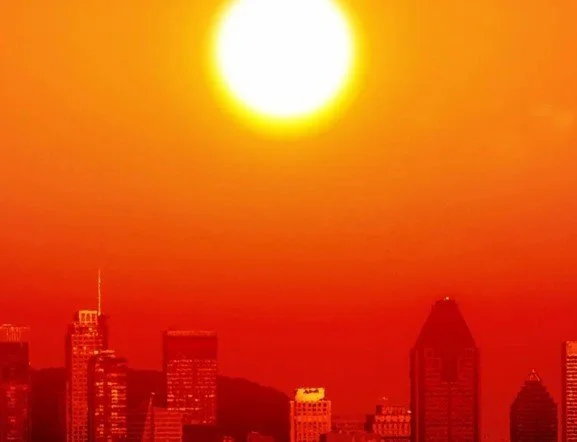 Sunset over a city skyline with tall buildings, with the sun shining brightly in the orange and yellow sky.