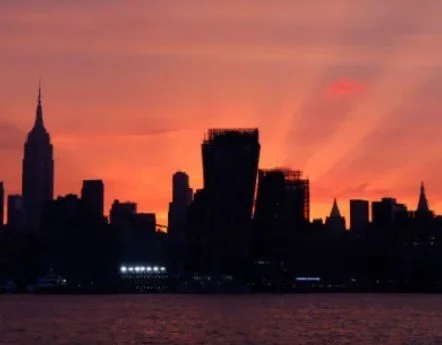 City skyline at sunset with silhouetted buildings and a body of water in the foreground.