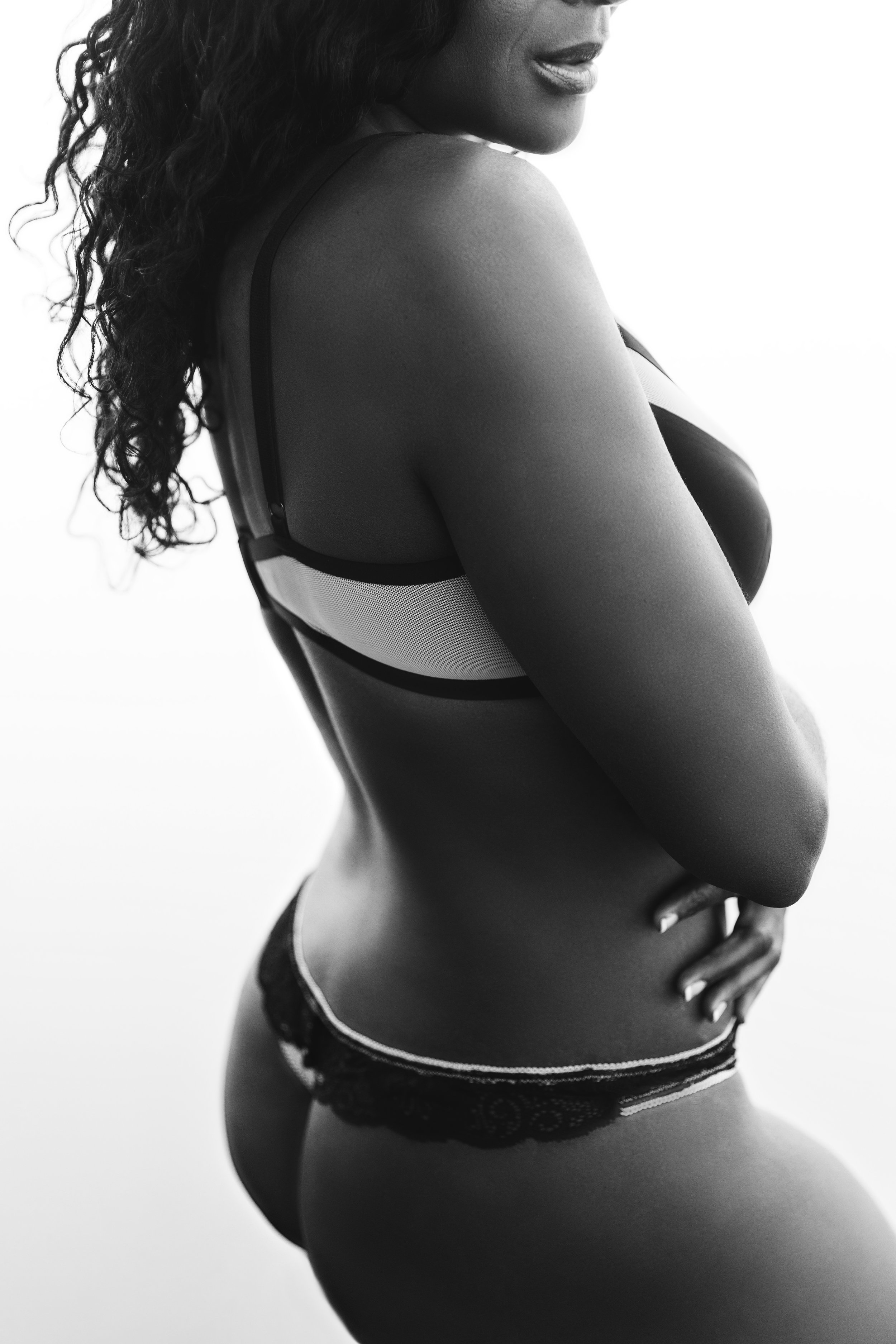 Black woman with long curls photographed from behind in black lace lingerie against a bright backdrop, black and white — Nashville boudoir portrait