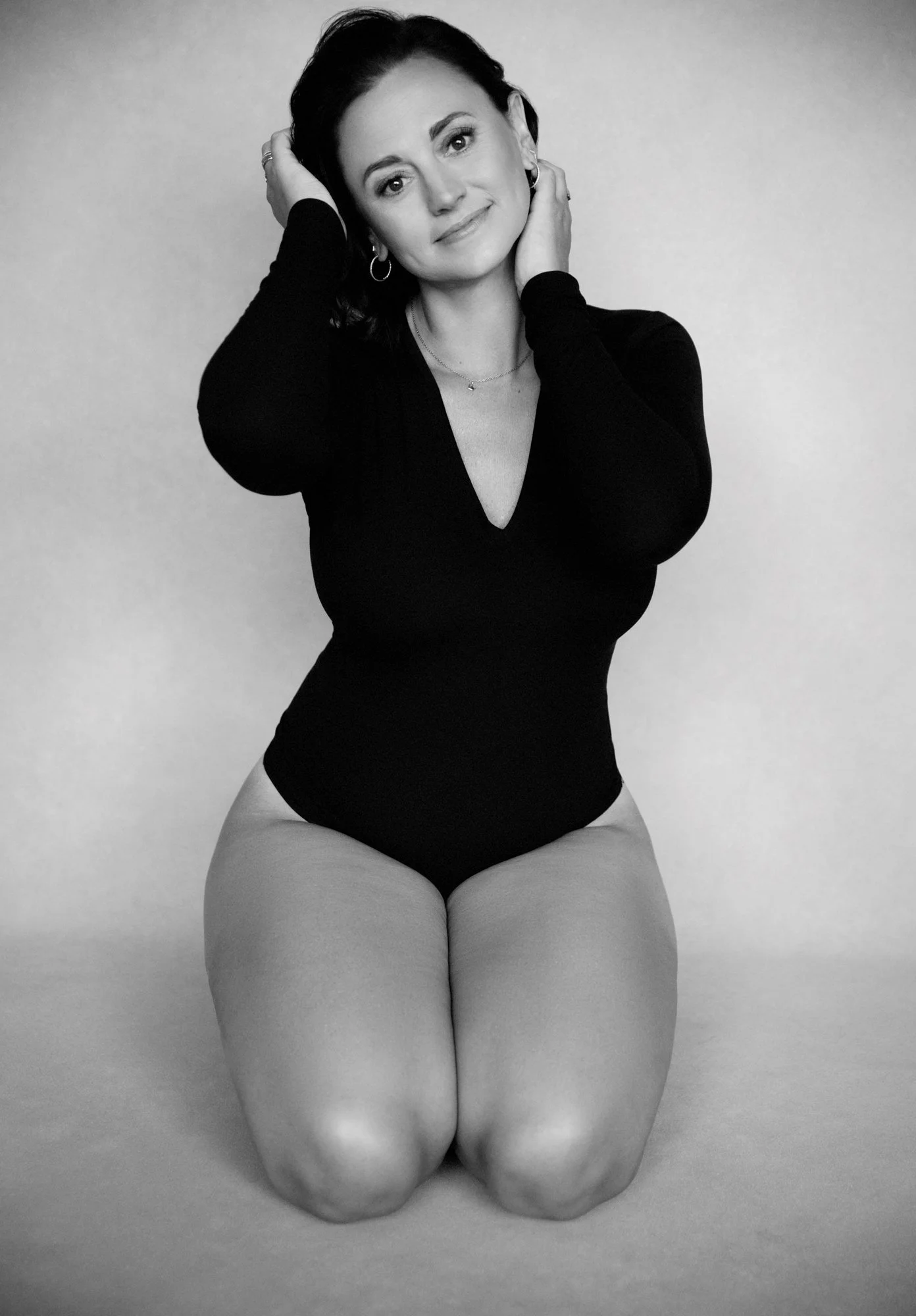  Black and white boudoir portrait on a seamless black drop of a woman in a black body suit. 