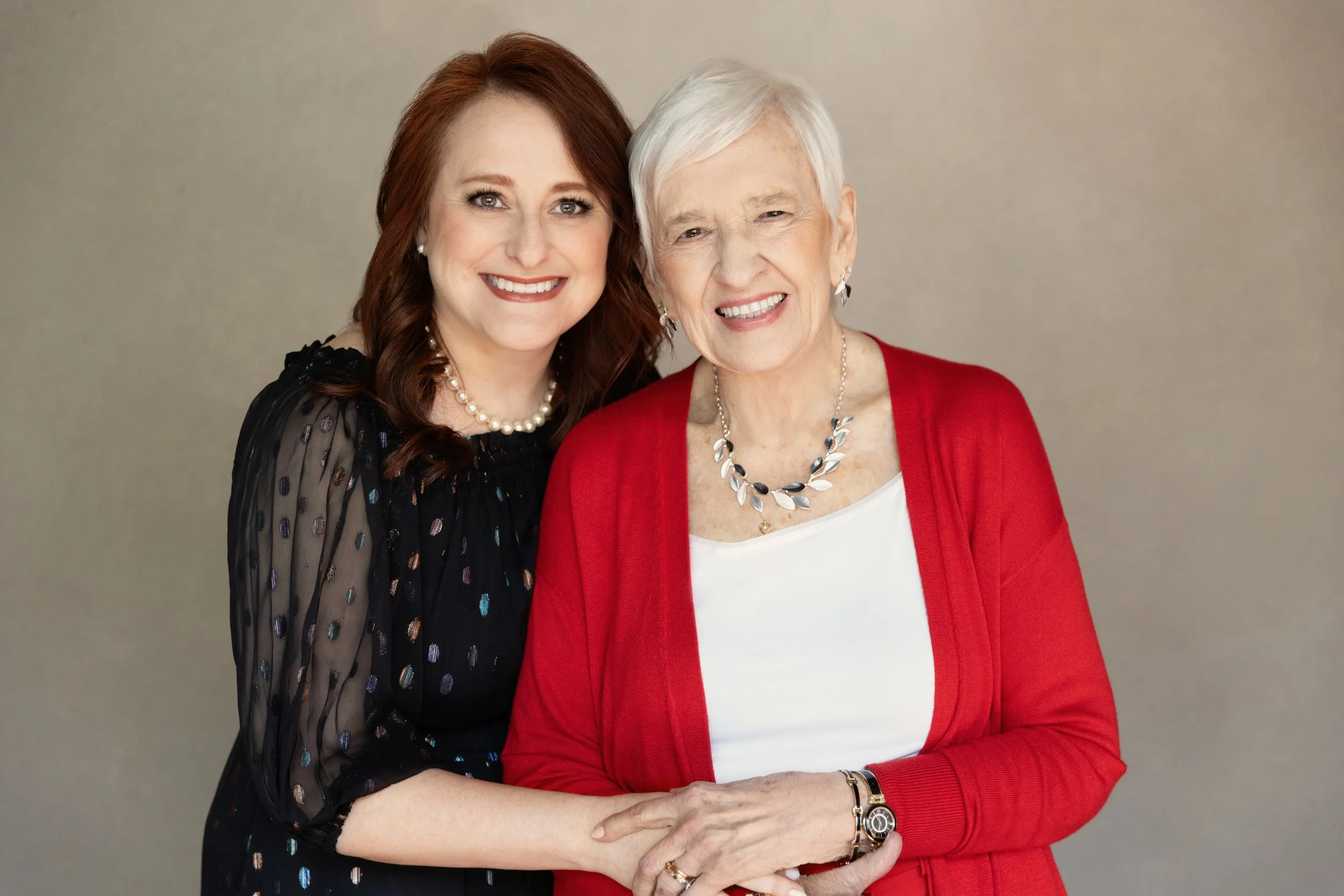  Daughter standing beside her elderly mother in a red cardigan, highlighting love and legacy in a generational family portrait. 