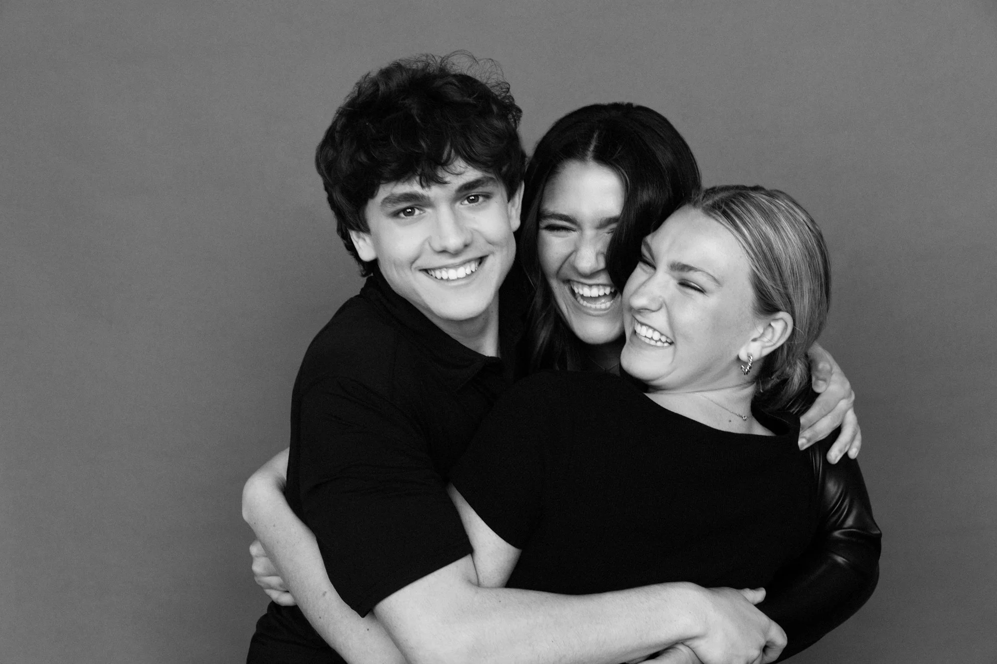  Three siblings hugging and laughing together in a candid black and white portrait, capturing playful connection during a family photoshoot. 