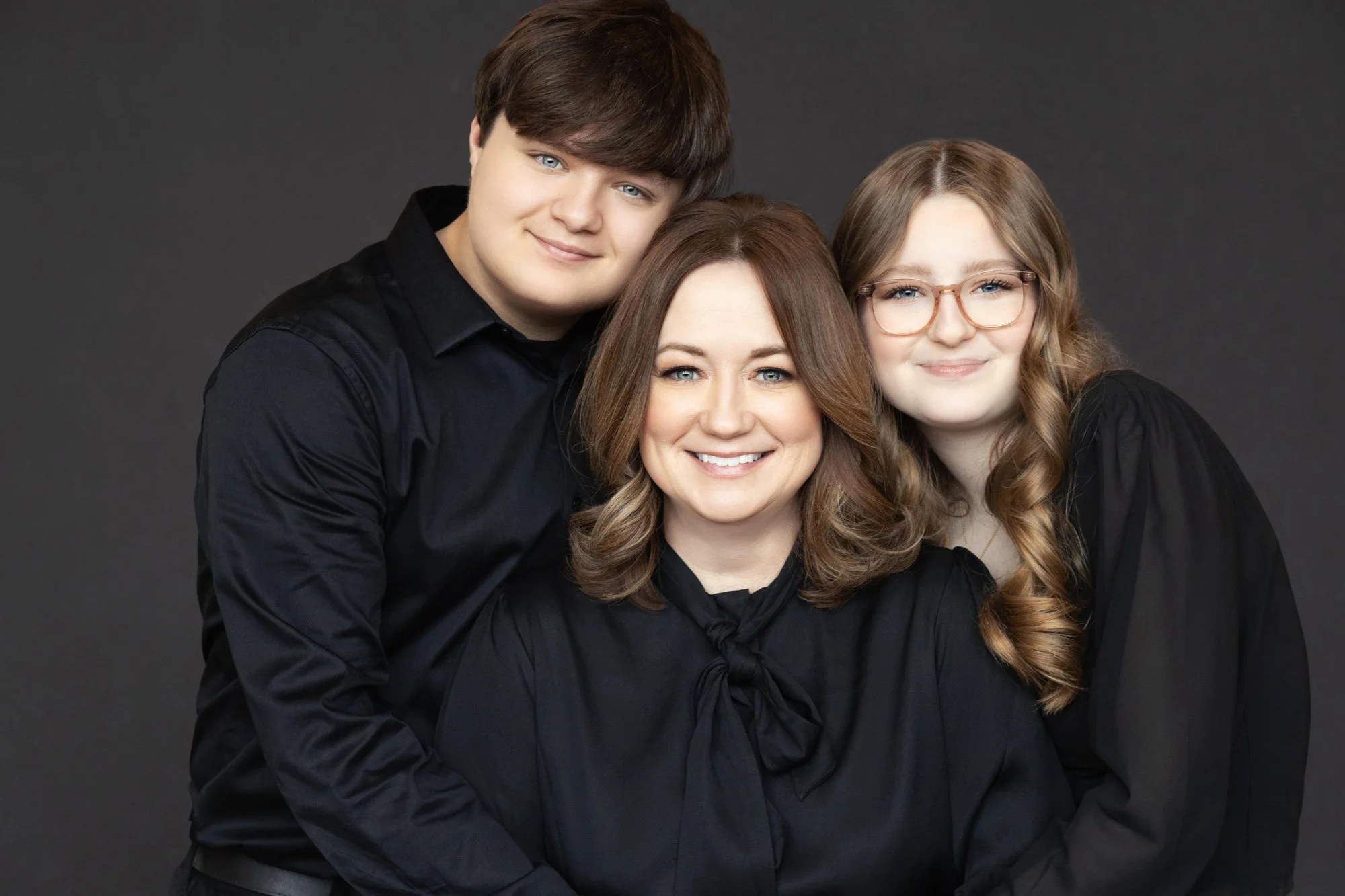  Mother seated with her teenage son and daughter leaning in close, capturing closeness and everyday connection in a family portrait. 