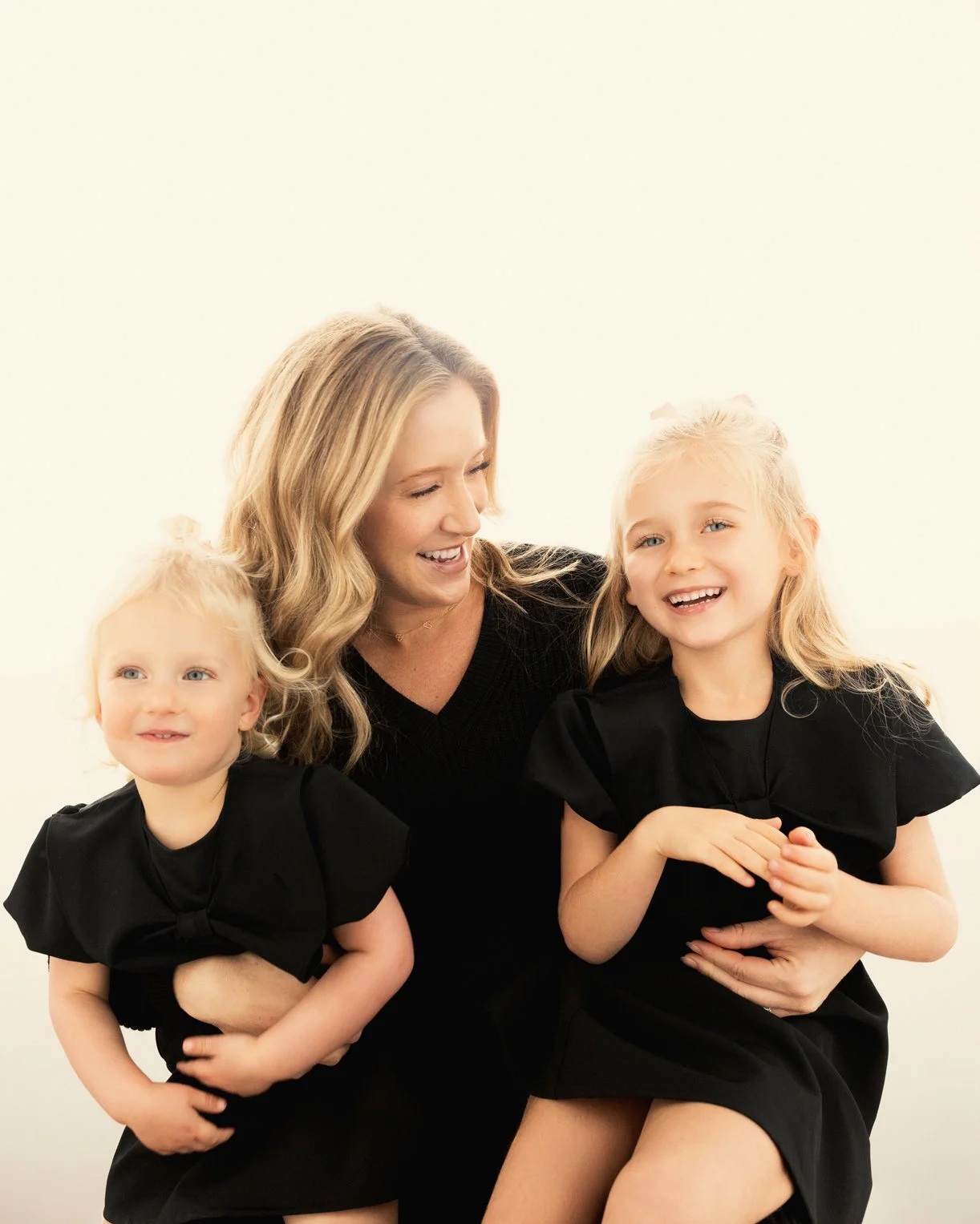  Mother laughing with her two young children dressed in black, showing playful connection and joy during a candid family photoshoot. 