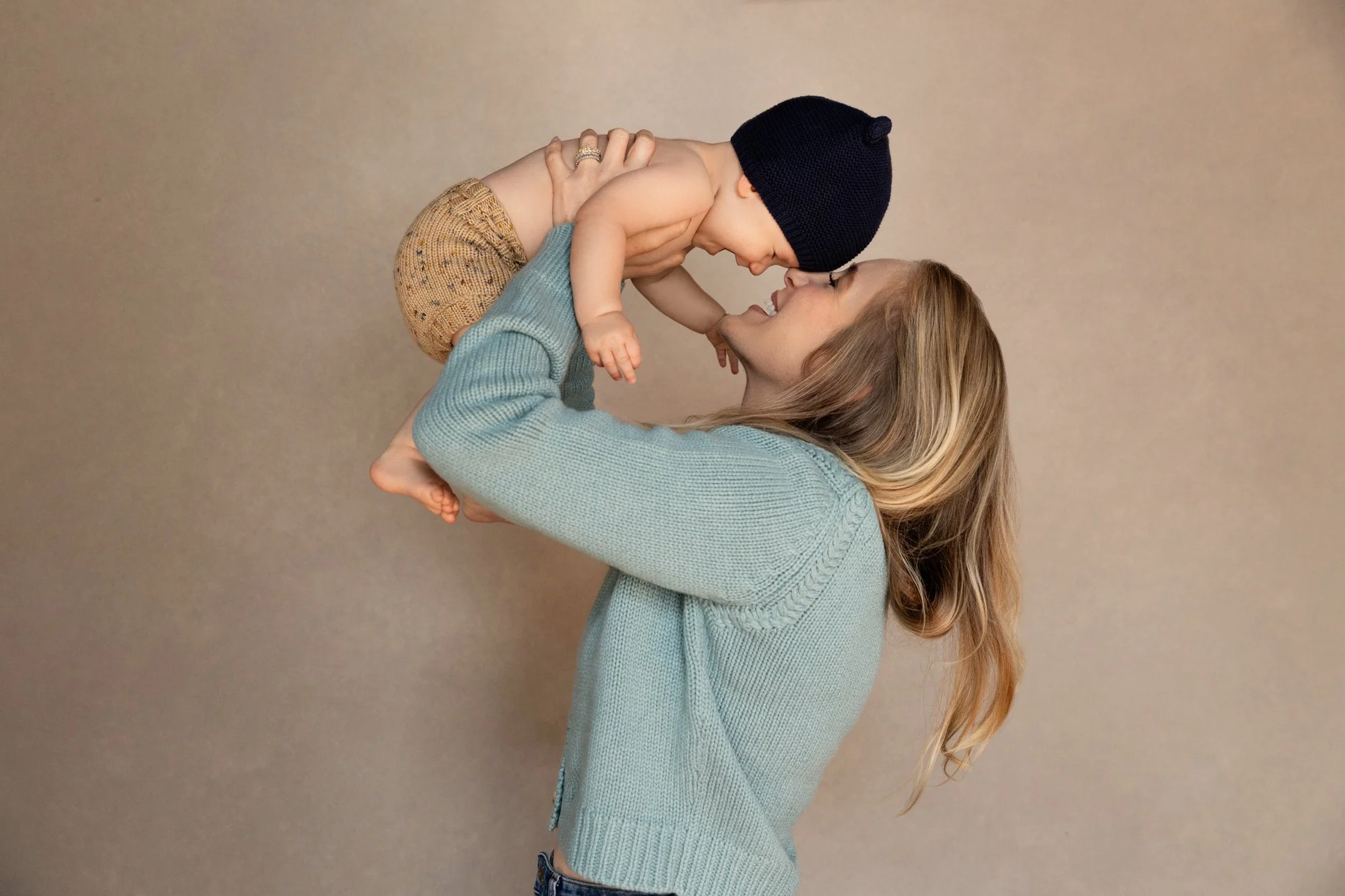  Mother lifting her baby in the air and smiling up at them, capturing a joyful and intimate moment in a family photography session. 