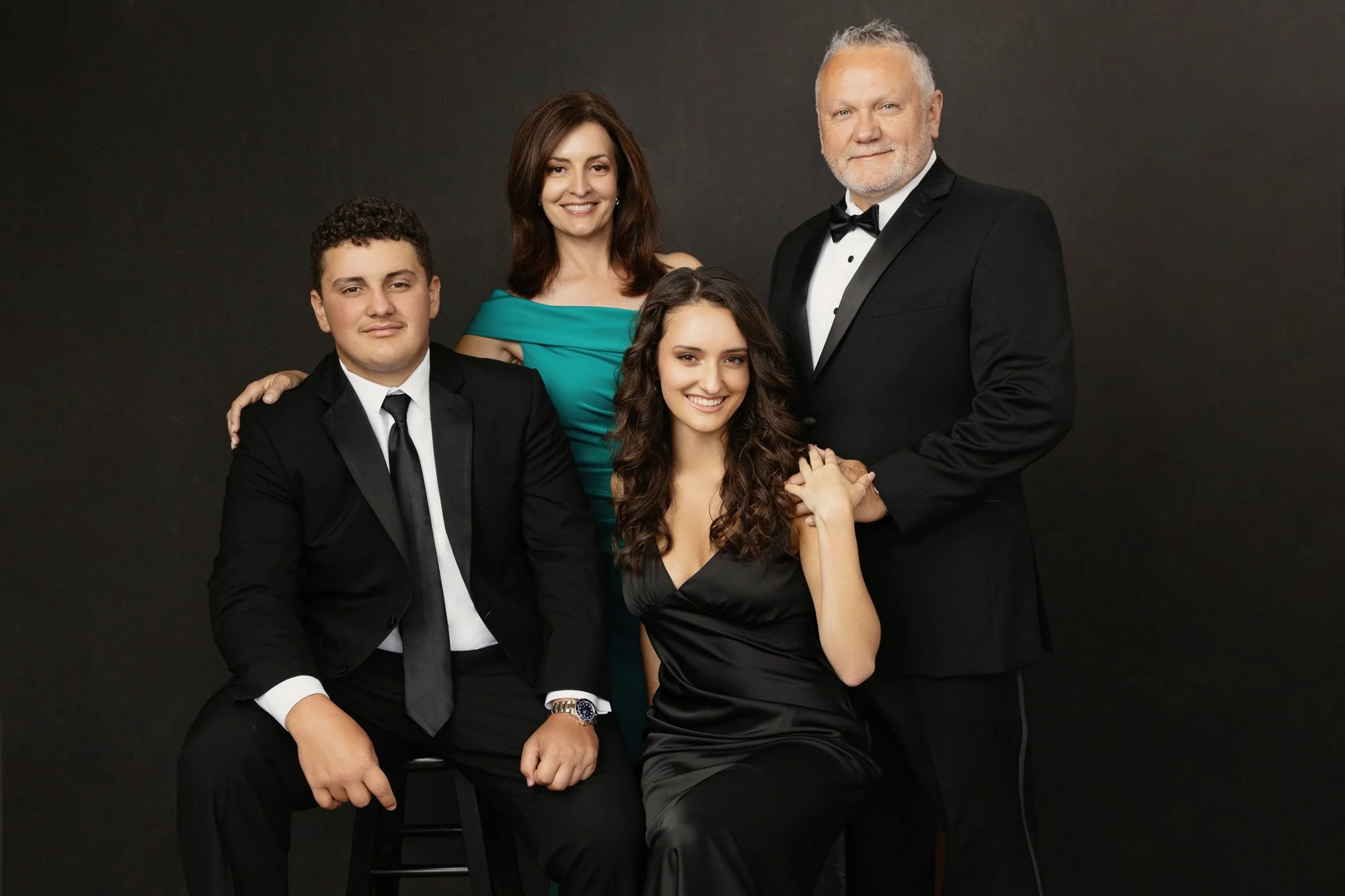 Formal family portrait with parents and two teenagers dressed in black and green, showing a polished and timeless family photoshoot. 