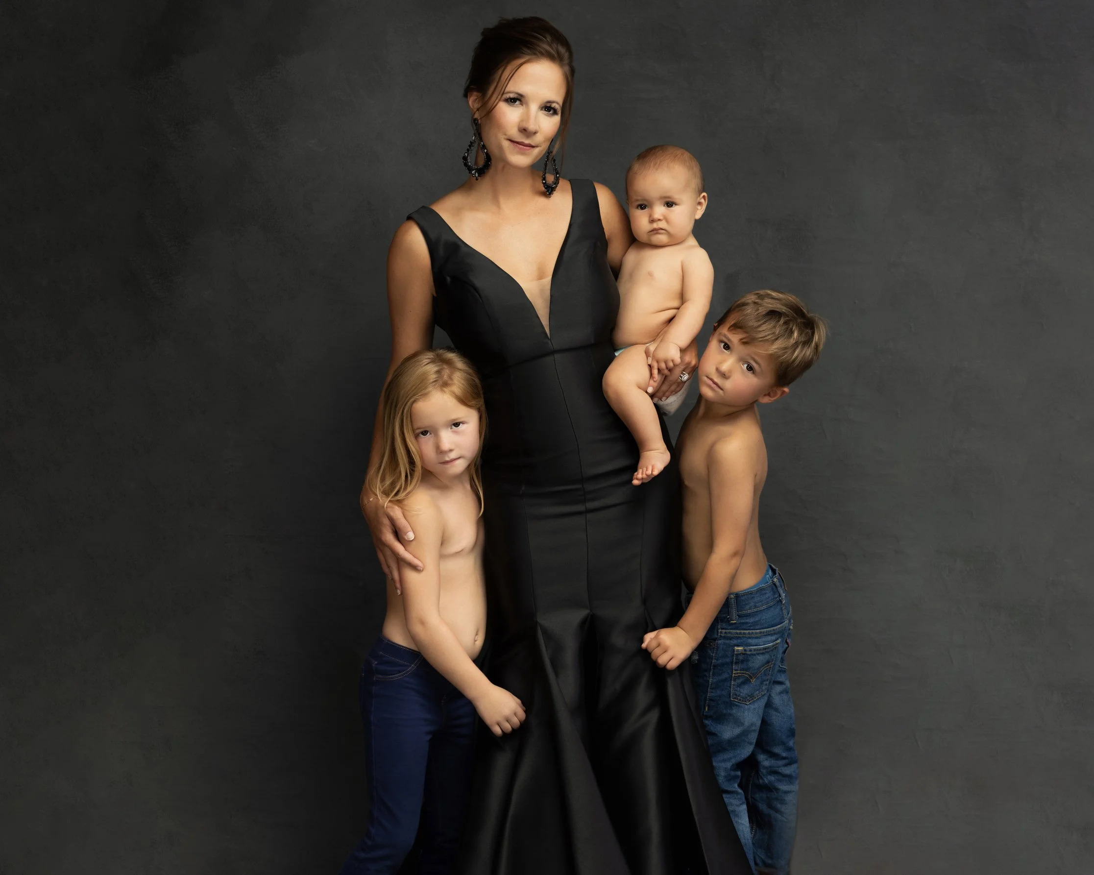  Mother standing with her three children including a baby in her arms, showing strength and connection in a timeless family portrait. 