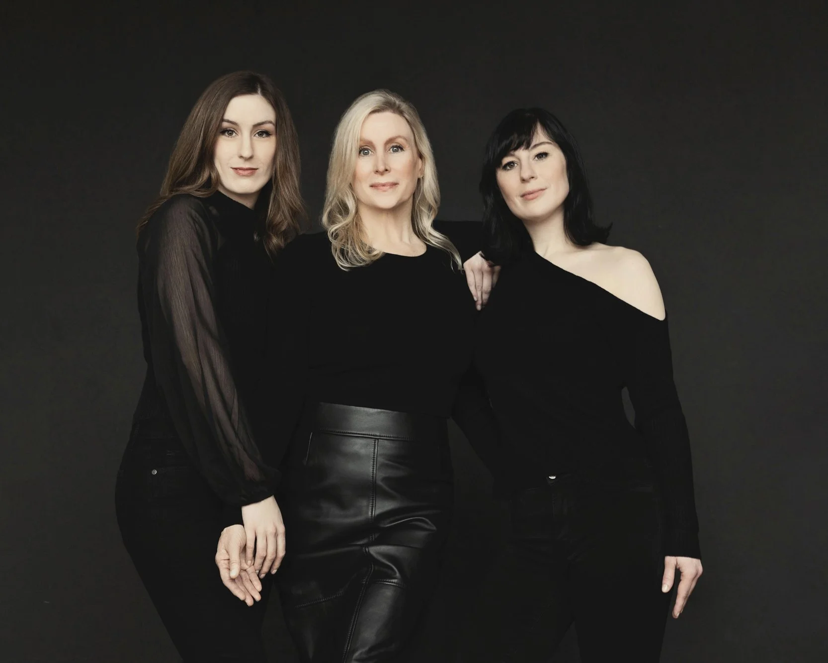  Three women dressed in black standing closely together, highlighting elegance and generational connection in a modern family portrait. 