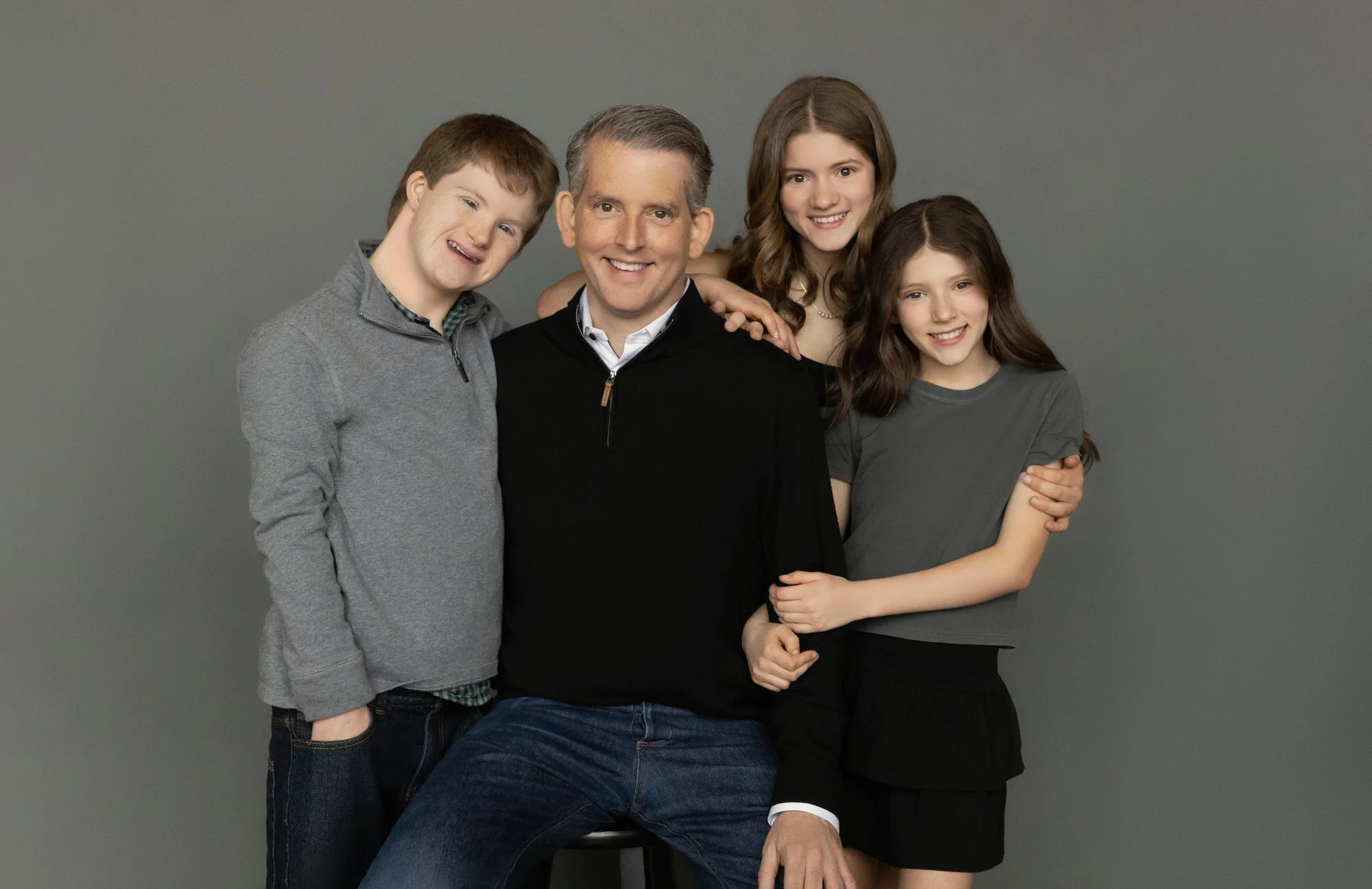  Father seated with his teenage son and two daughters gathered around him, capturing a warm and connected family photoshoot. 
