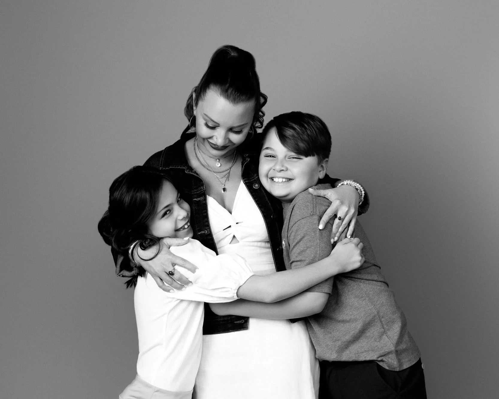  Mother hugging her two young children in a black and white portrait, capturing affection and closeness in a candid family photoshoot. 