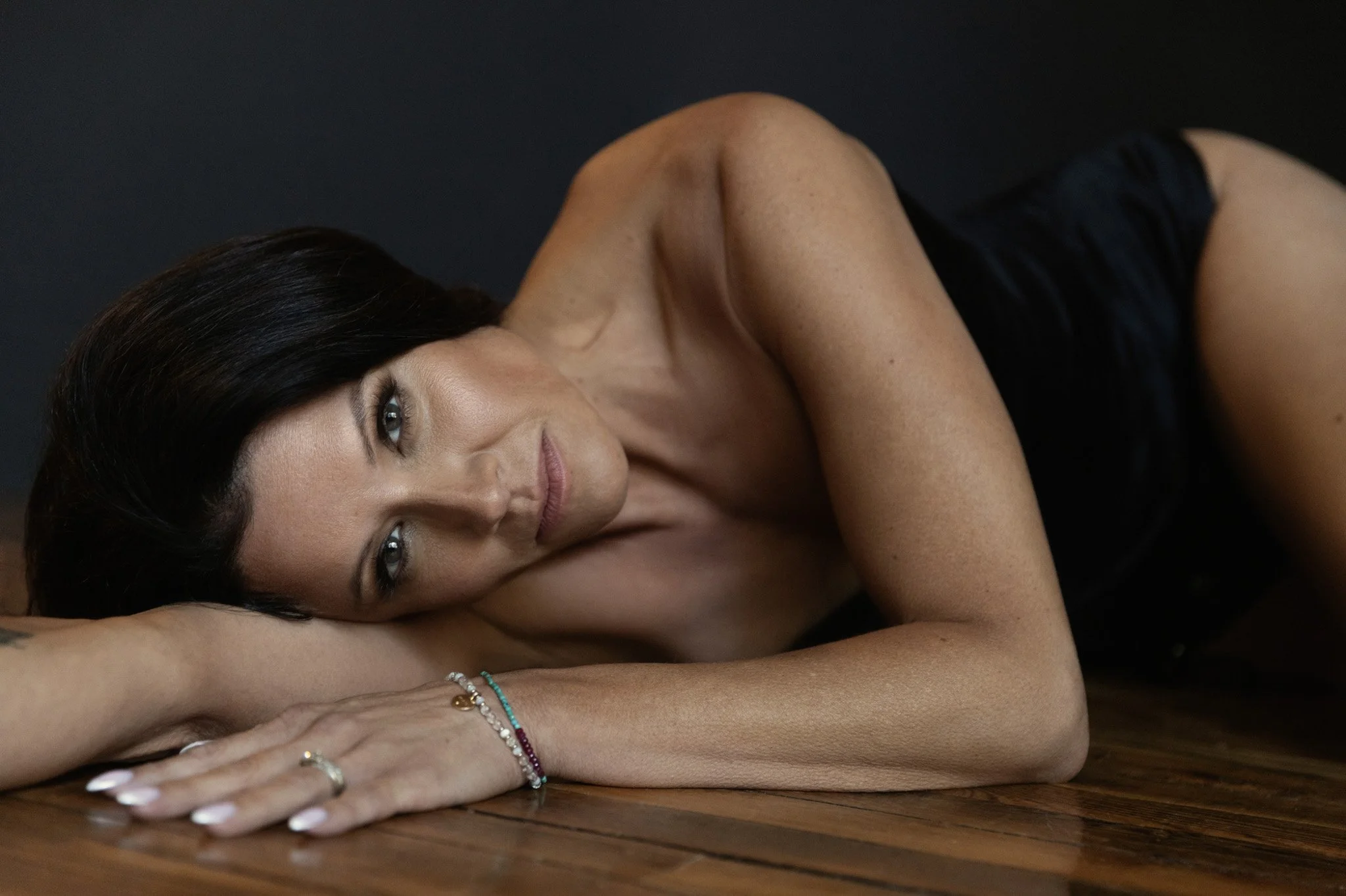 Brunette woman resting her head on her arm on a hardwood floor, bare shoulders and delicate bracelets — Nashville boudoir photography