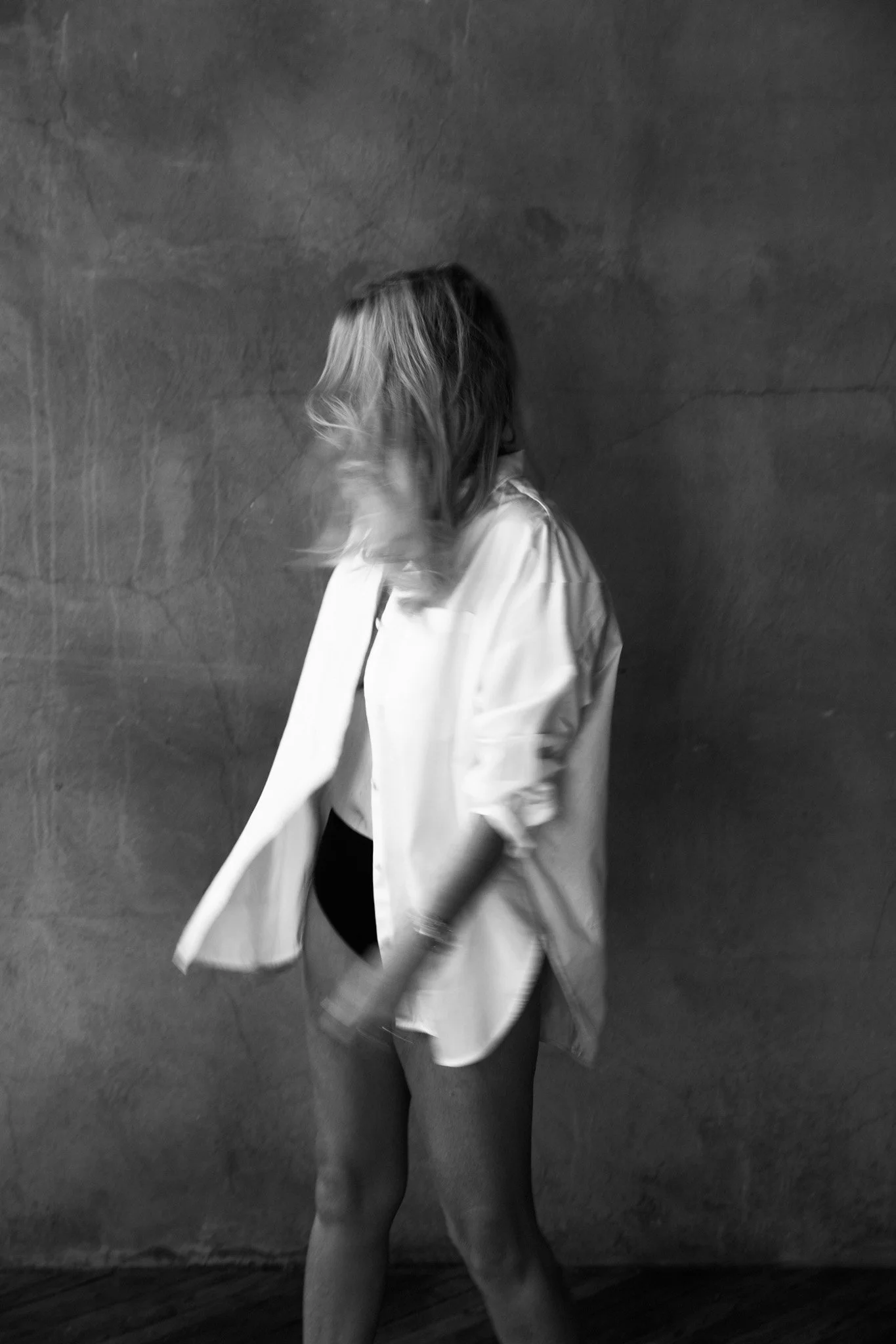 Blonde woman in an open white shirt captured in motion against a concrete wall, black and white — Nashville boudoir portrait