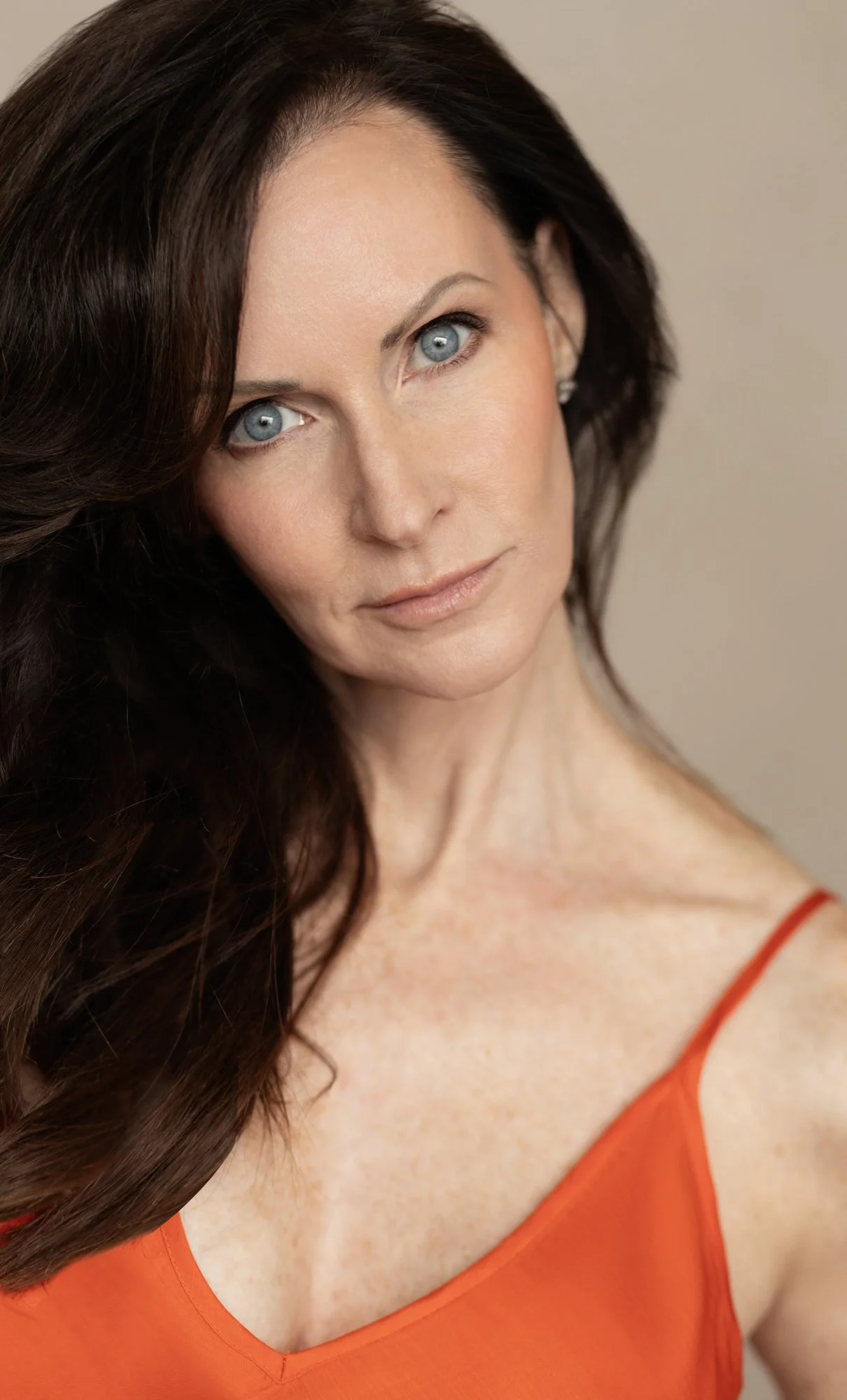 Brunette woman with blue eyes in an orange top, Nashville beauty portrait by Judith Hill