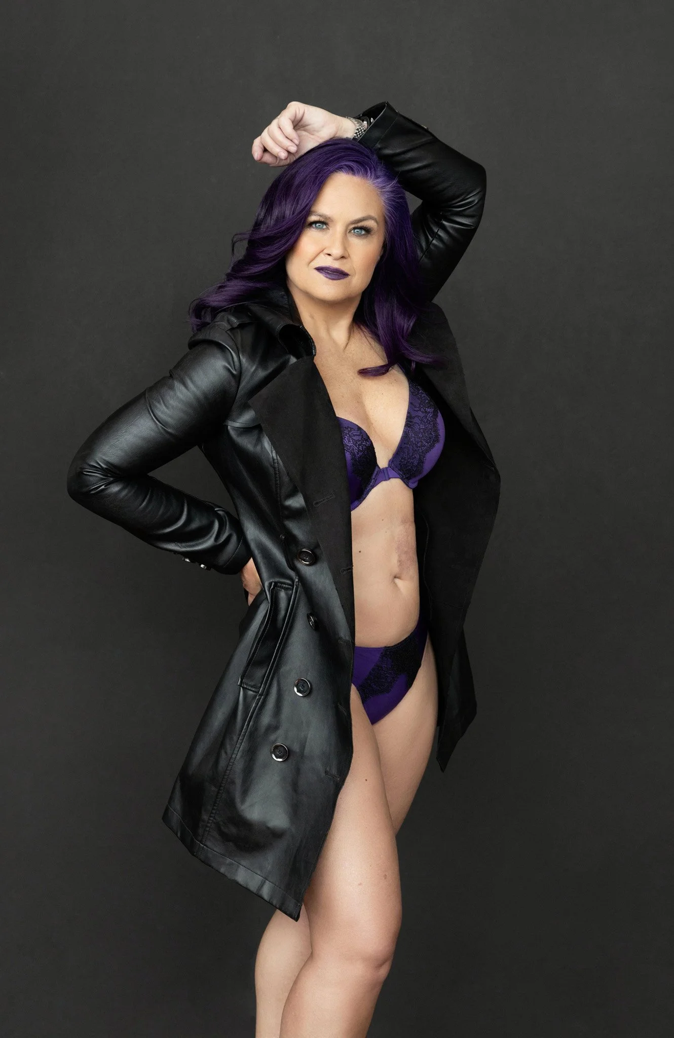 Woman with vibrant purple hair in a black leather trench coat over purple lingerie, bold and confident — Nashville boudoir photography