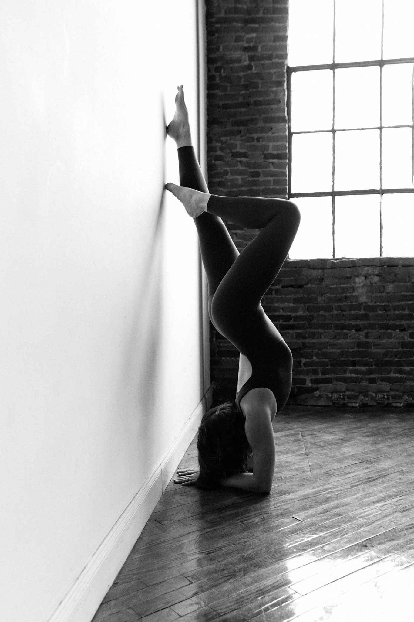 Woman in a forearm stand against a white wall beside a warehouse window, athletic black and white — Nashville boudoir portrait 