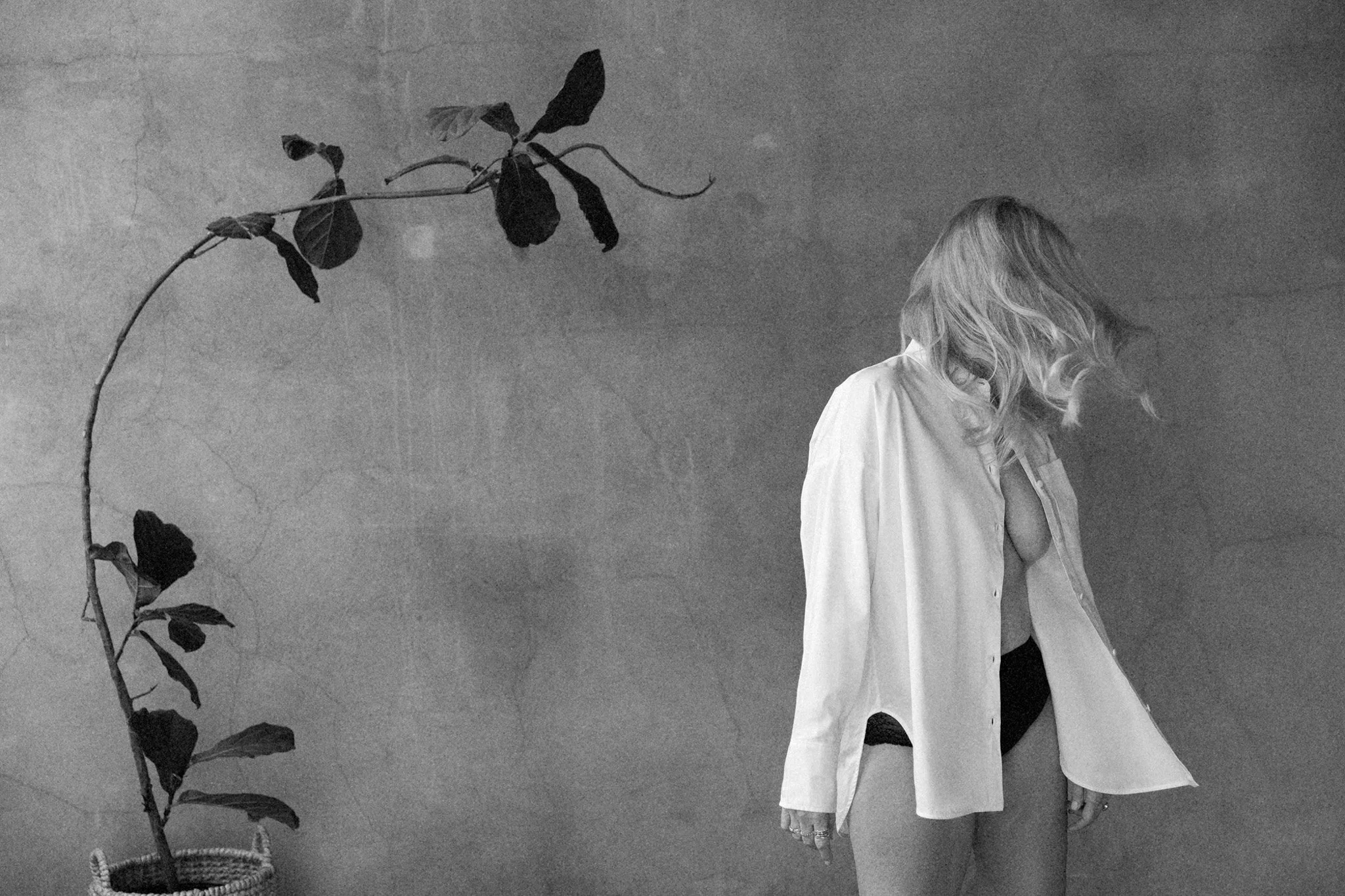 Blonde woman seen from behind in an open white shirt beside a leafy plant against a concrete wall, black and white — Nashville boudoir portrait