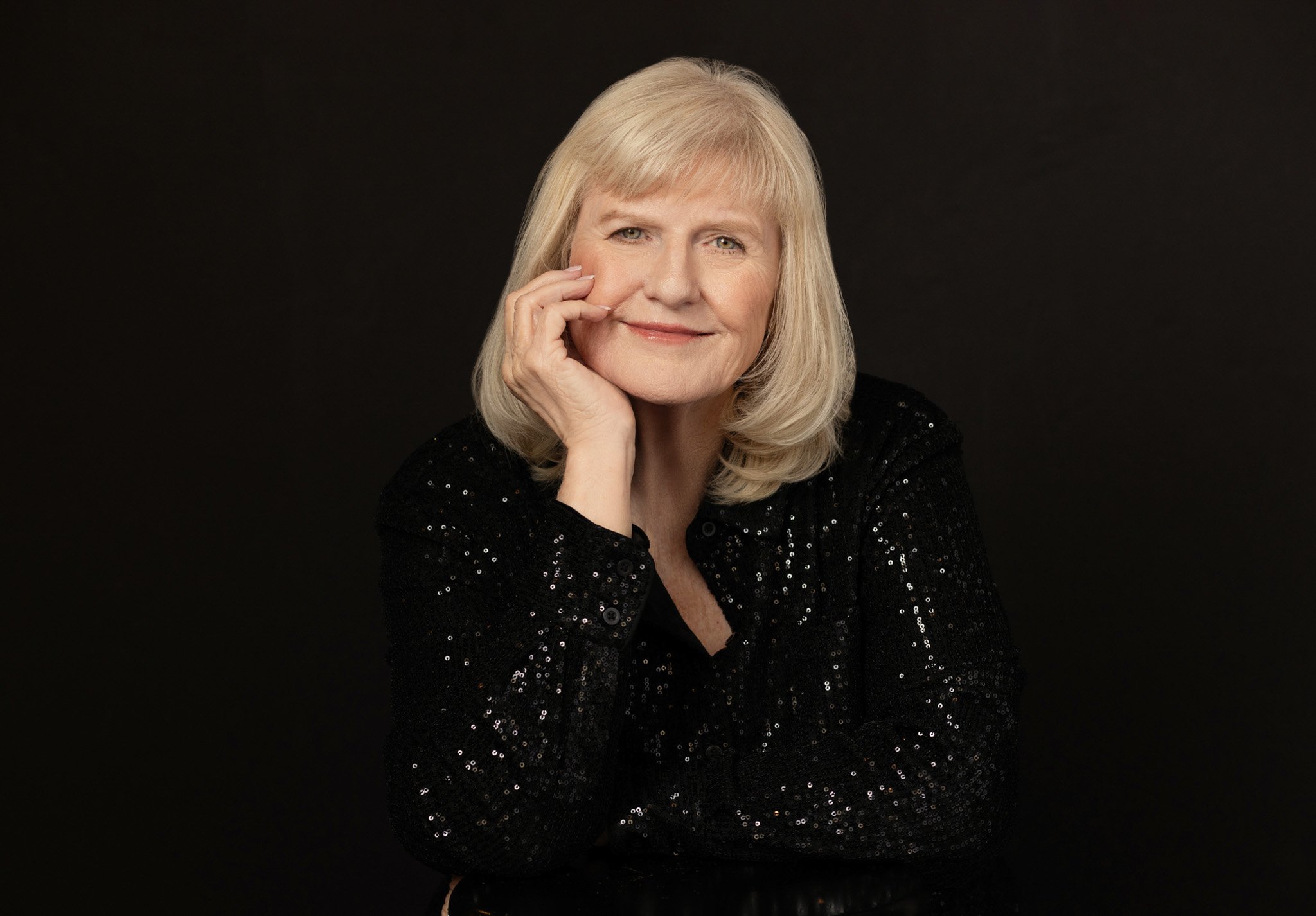 Silver-blonde woman in a black sequin top resting her chin on her hand, Nashville studio portrait by Judith Hill