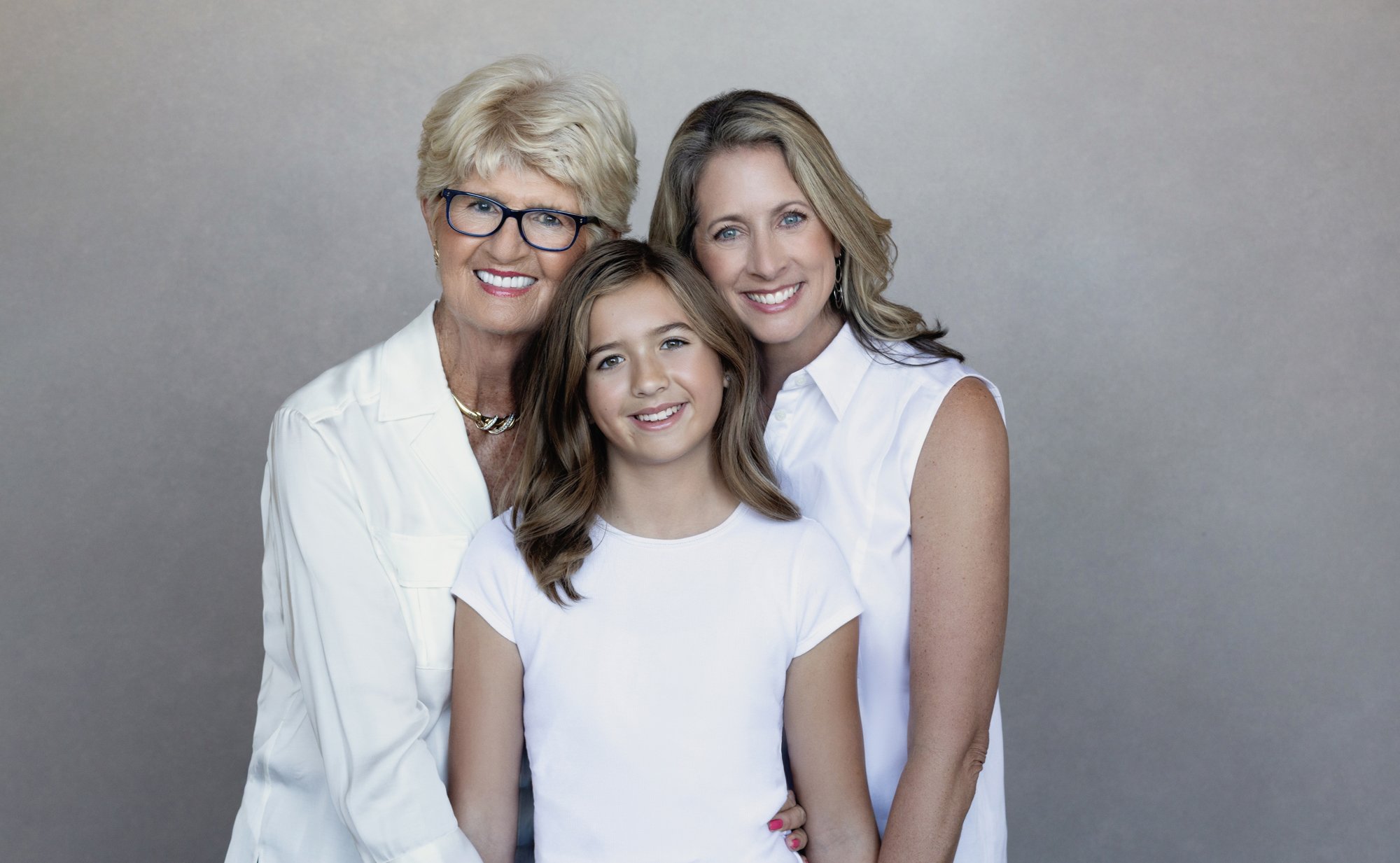 Three generations of women smiling together in soft neutral tones, capturing connection and legacy through a generational photoshoot.