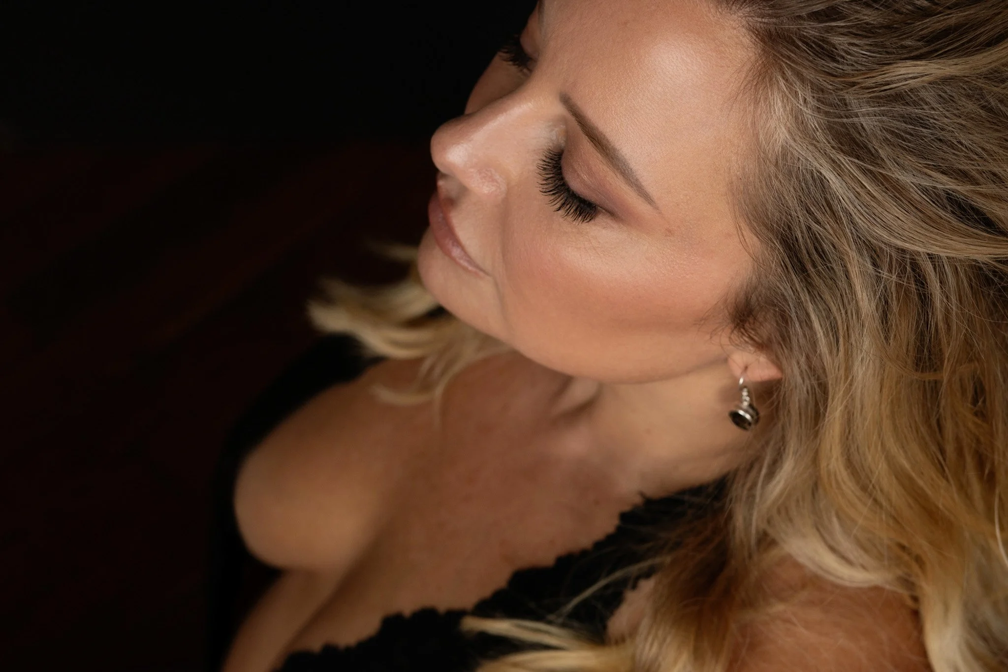 Intimate warm-light close-up of a blonde woman with eyes closed wearing black lace — Nashville boudoir photography