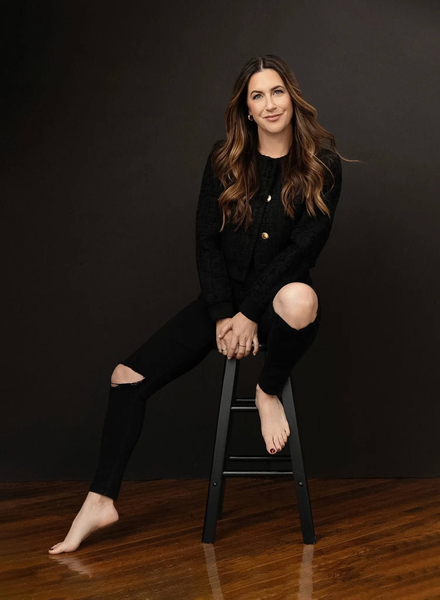 Woman in a black jacket and ripped jeans seated on a stool, Nashville lifestyle portrait by Judith Hill