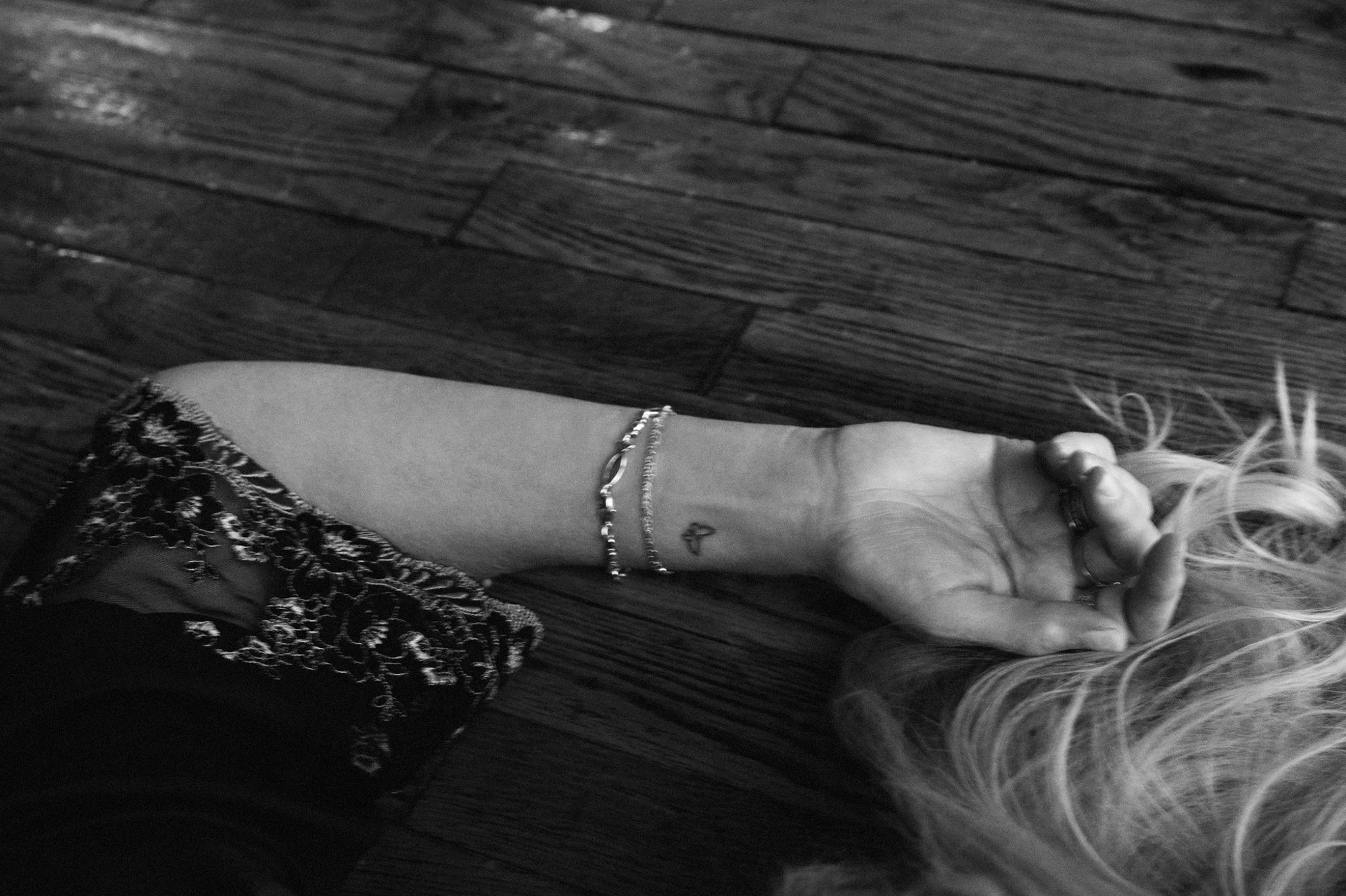 Black and white detail of a woman's outstretched arm on a wood floor with bracelets and a small heart tattoo — Nashville boudoir