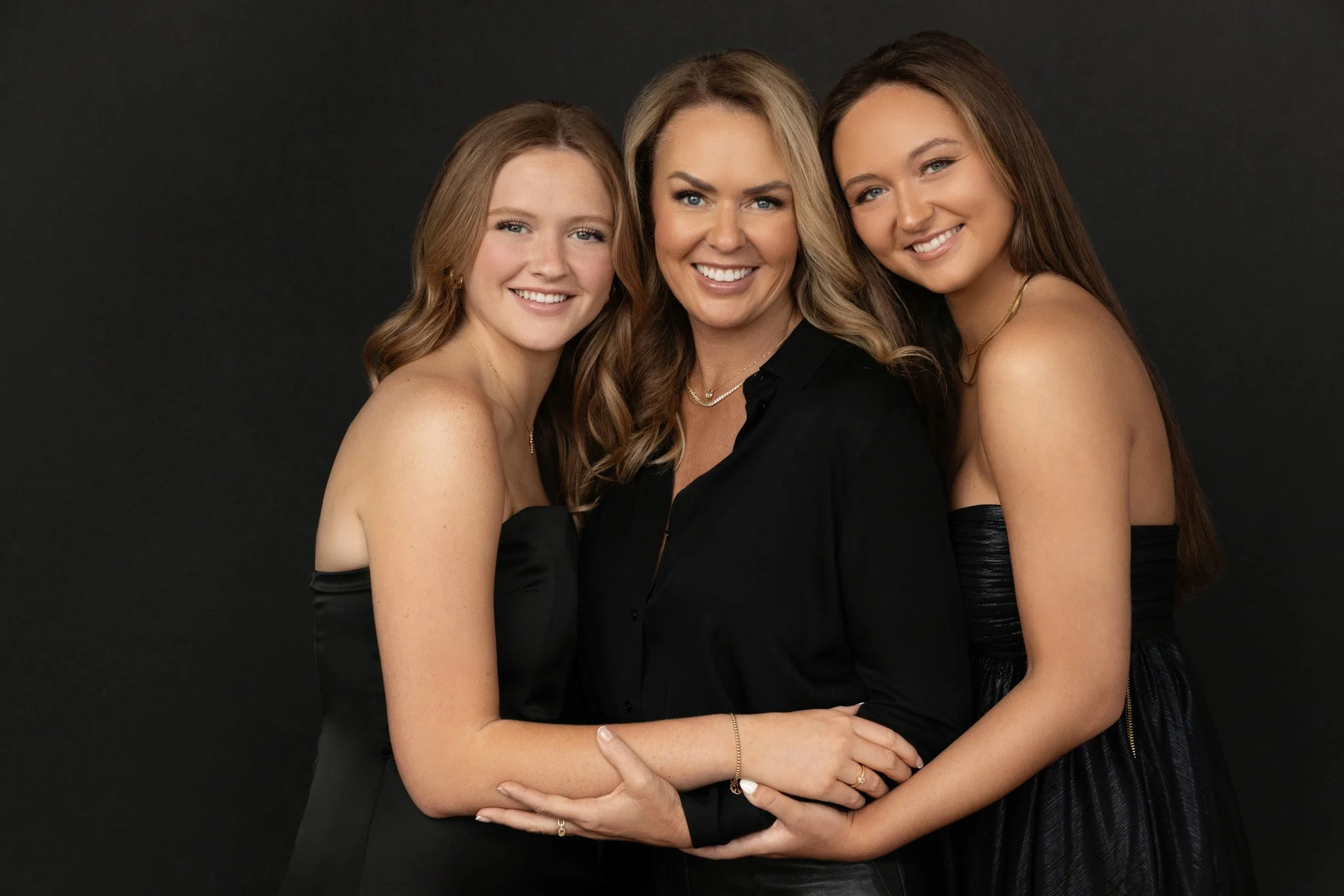 Mother and her two teenage daughters in black outfits embracing and smiling together, Nashville studio family portrait by Judith Hill