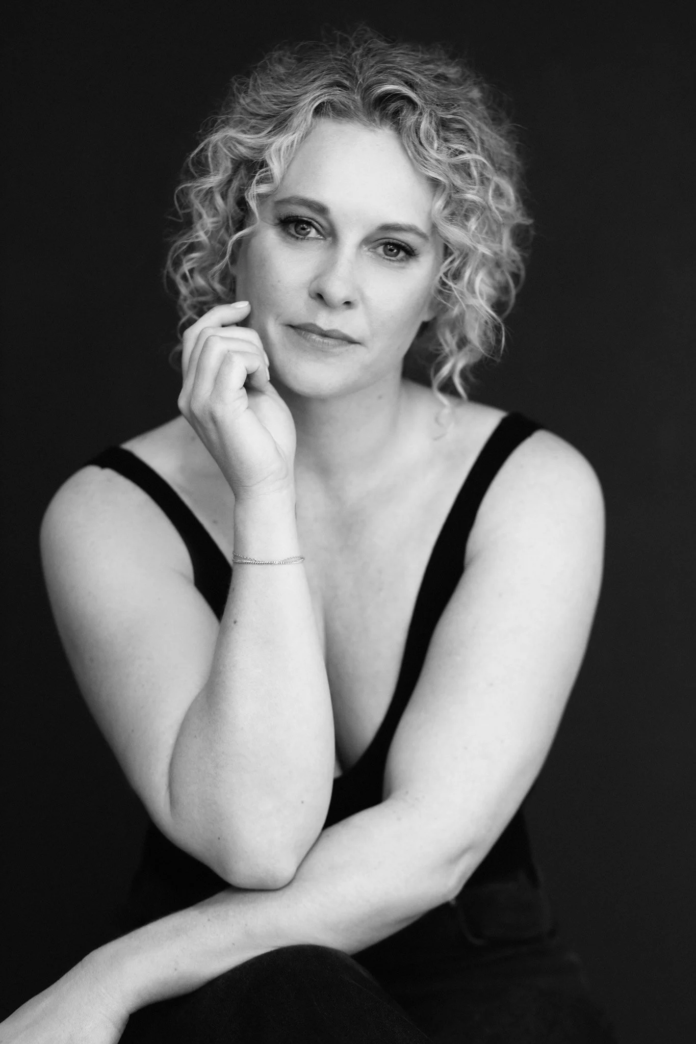 Black-and-white portrait of a woman with curly hair resting her chin on her hand, Nashville studio portrait by Judith Hill