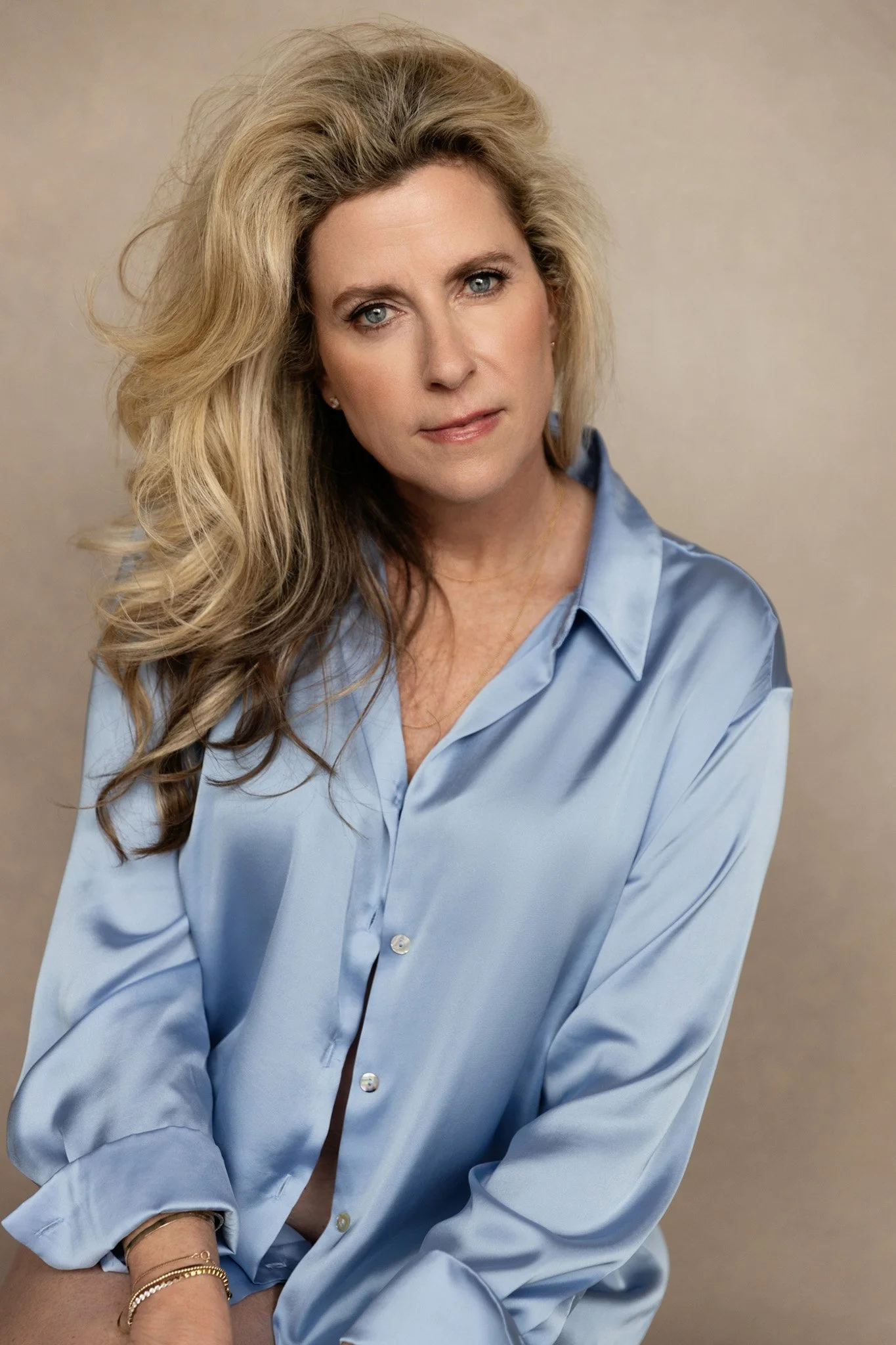 Blonde woman in a blue silk button-down shirt with soft waves against a neutral backdrop — Nashville boudoir photography