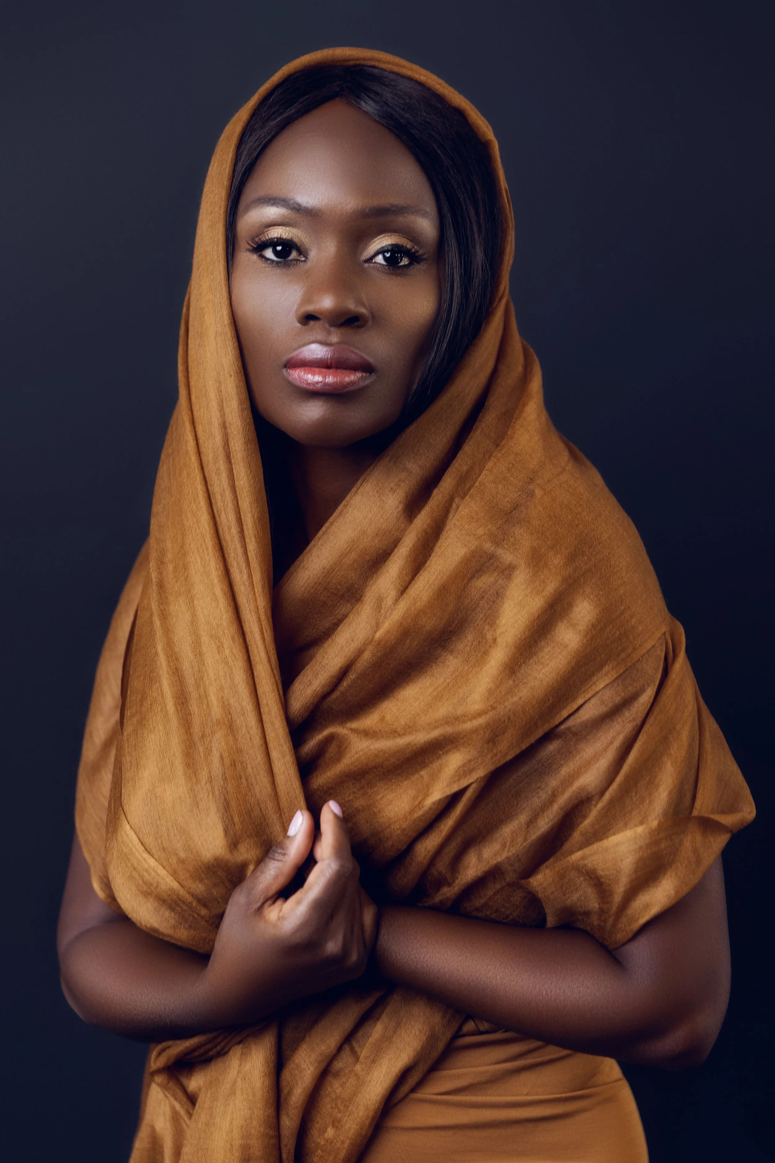 Dark-haired black woman wrapped in a flowing ochre scarf clasping her hands at her chest, Nashville studio portrait by Judith Hill