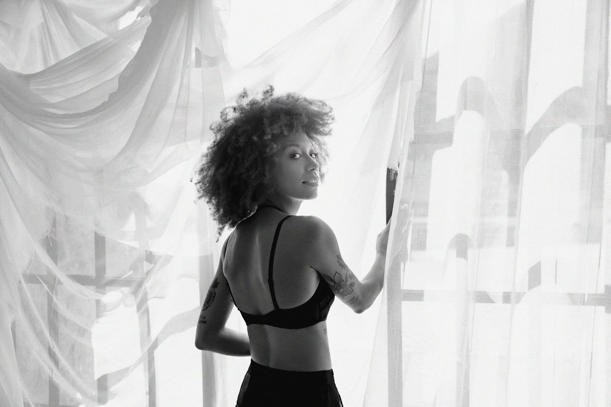 Black-and-white boudoir portrait of a woman glancing over her shoulder, backlit among sheer white draped curtains — Judith Hill Photography, Nashville