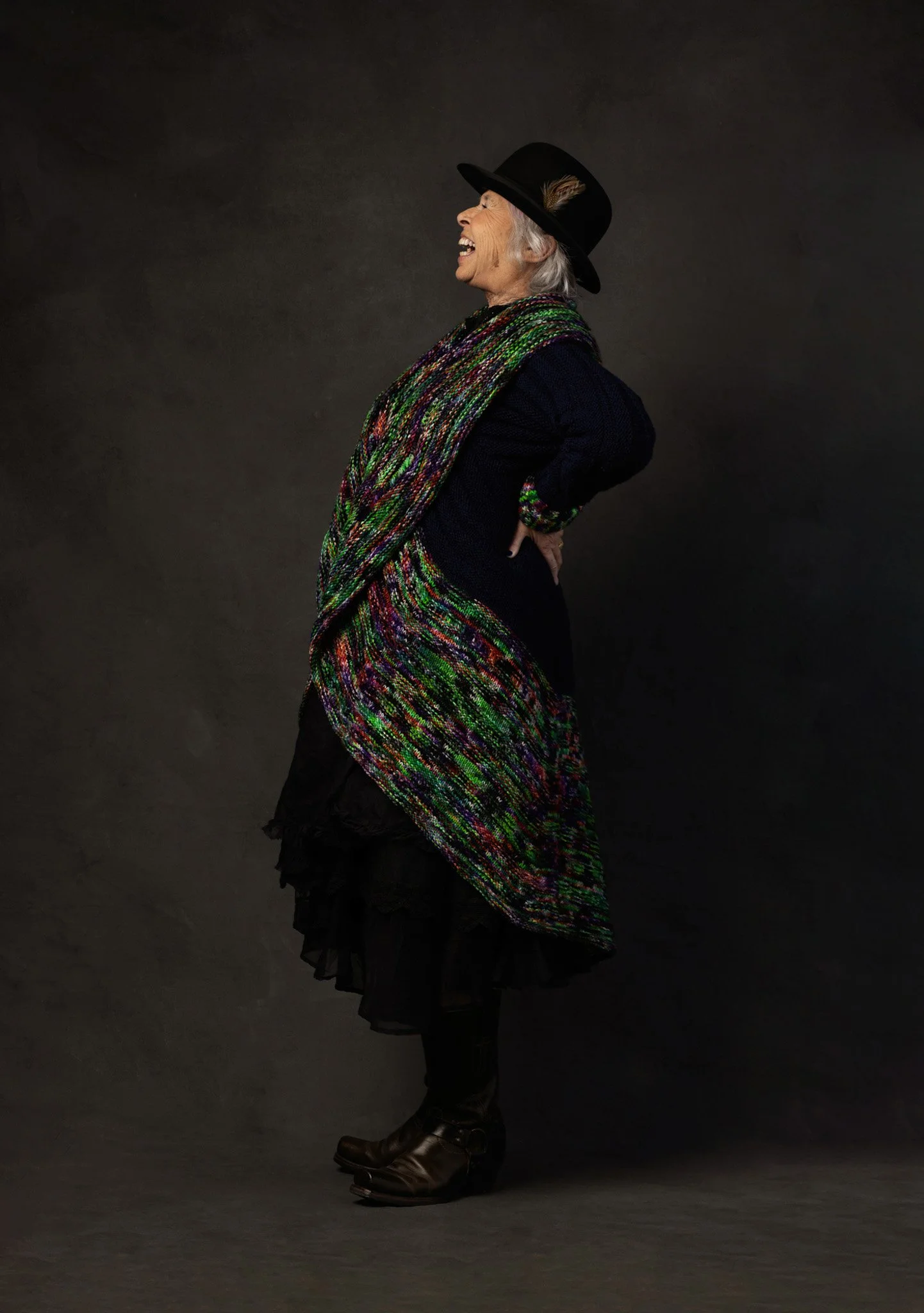Older woman laughing in a black hat and colorful knit scarf, Nashville character portrait by Judith Hill