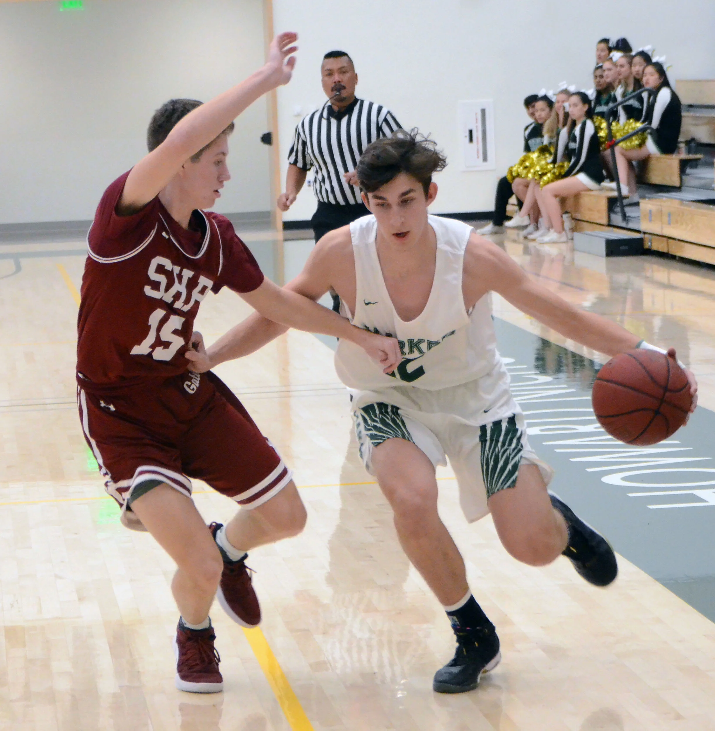 A Harker basketball player dribbles past a defender from Sacred Heart. Head of Upper School Butch Keller coaches the varsity boys basketball team. Photo by Eric Fang