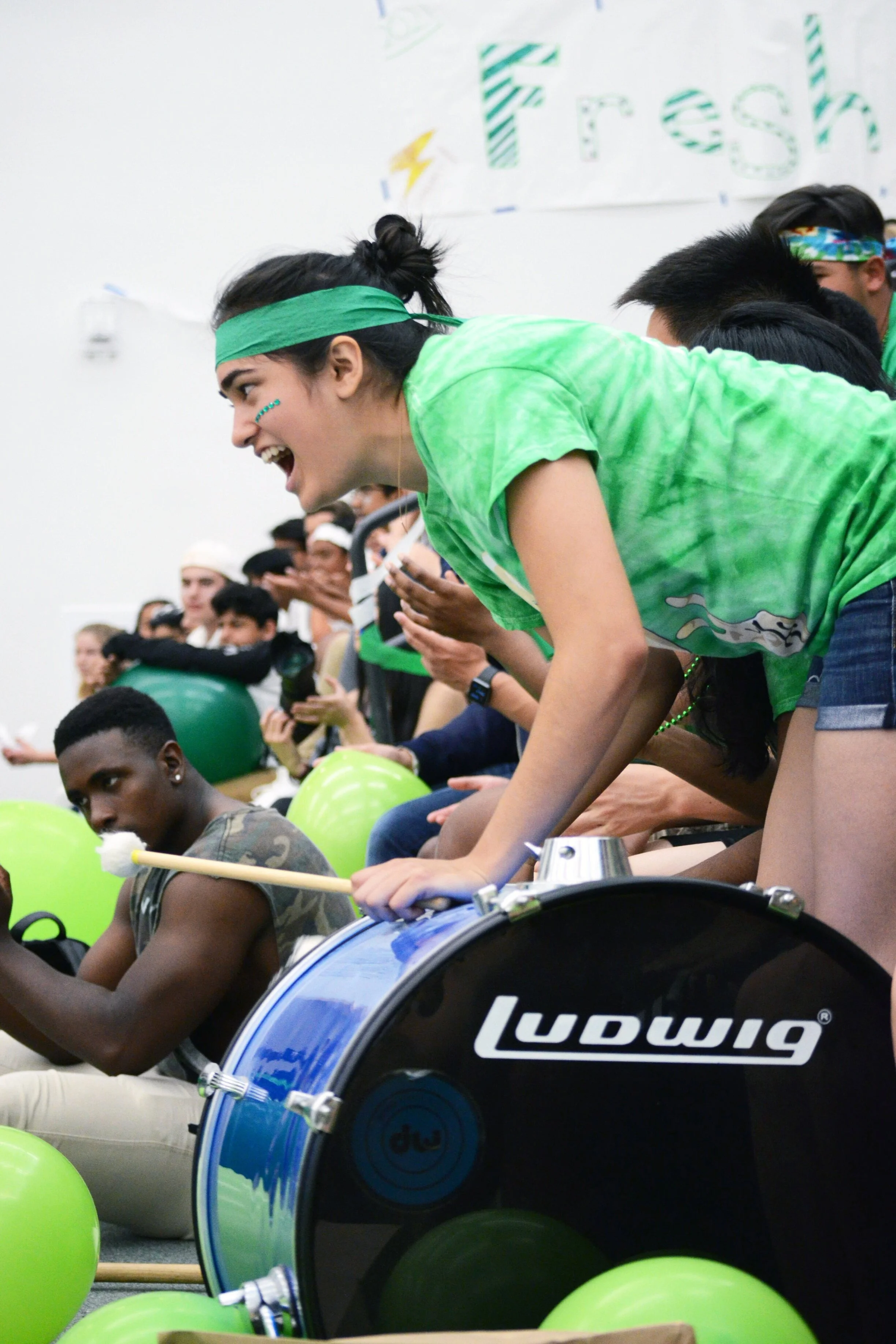 A senior plays a large drum to energize her class. The senior class’s class color is green. Photo by Eric Fang