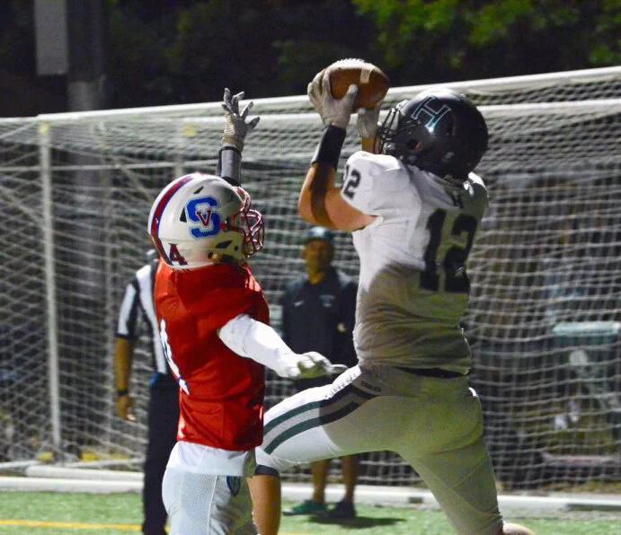 A Harker receiver catches the football and scores a touchdown, narrowly evading an opposing defender at Harker’s Homecoming game against St. Vincent de Paul. Harker merged their varsity and junior varsity teams for the 2018-2019 season. Photo by Eri…