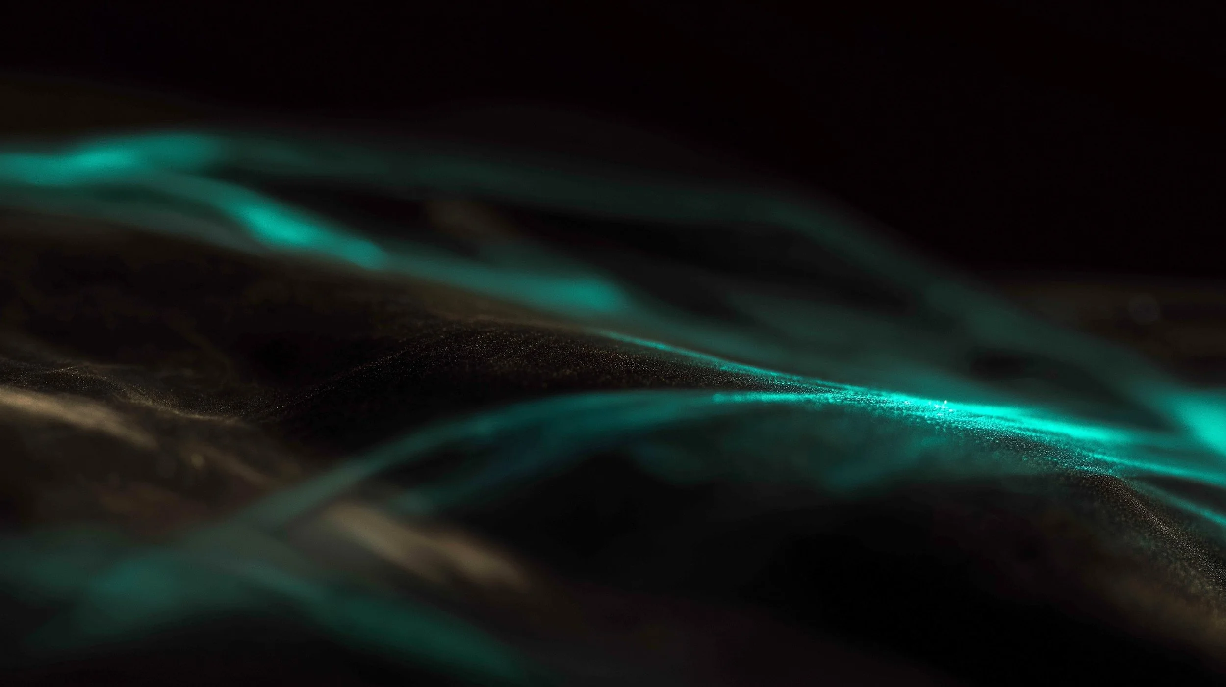 Close-up image of glowing blue-green fiber optic strands in darkness.
